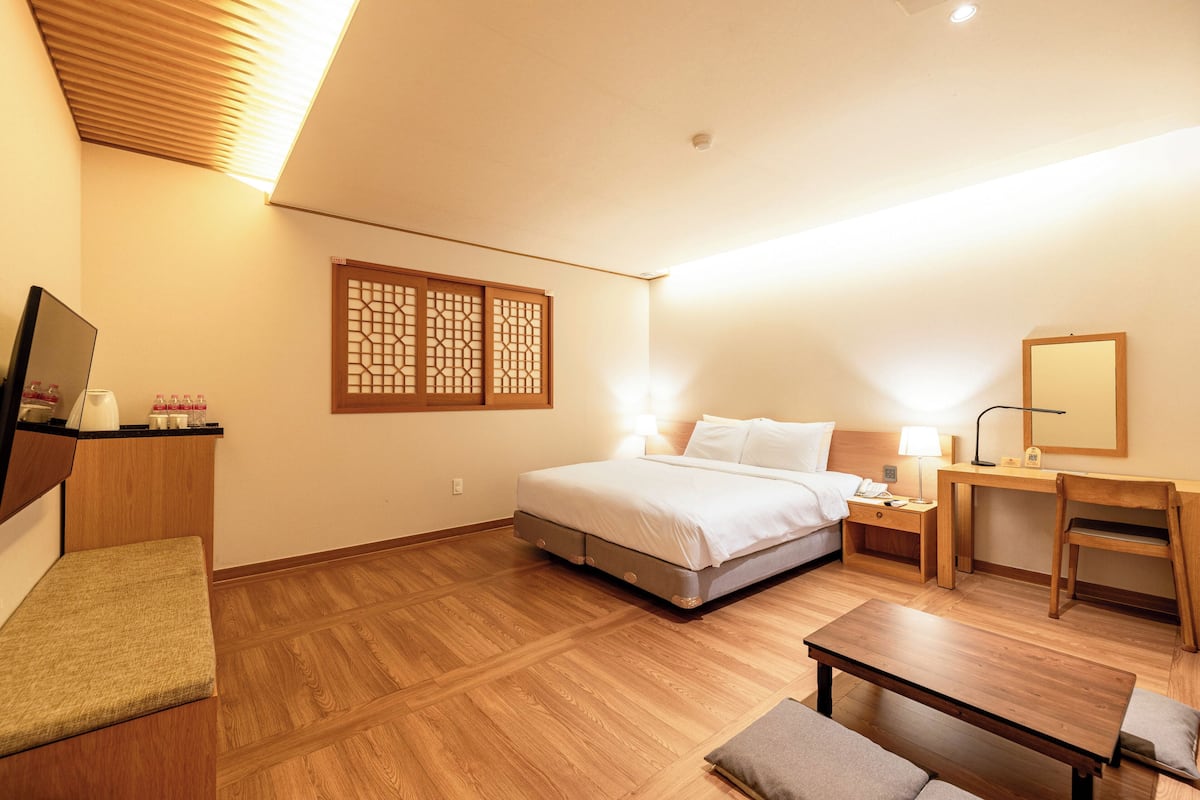 A hotel room with a bed, bedside table, lamp, chair, and a small desk with a mirror.