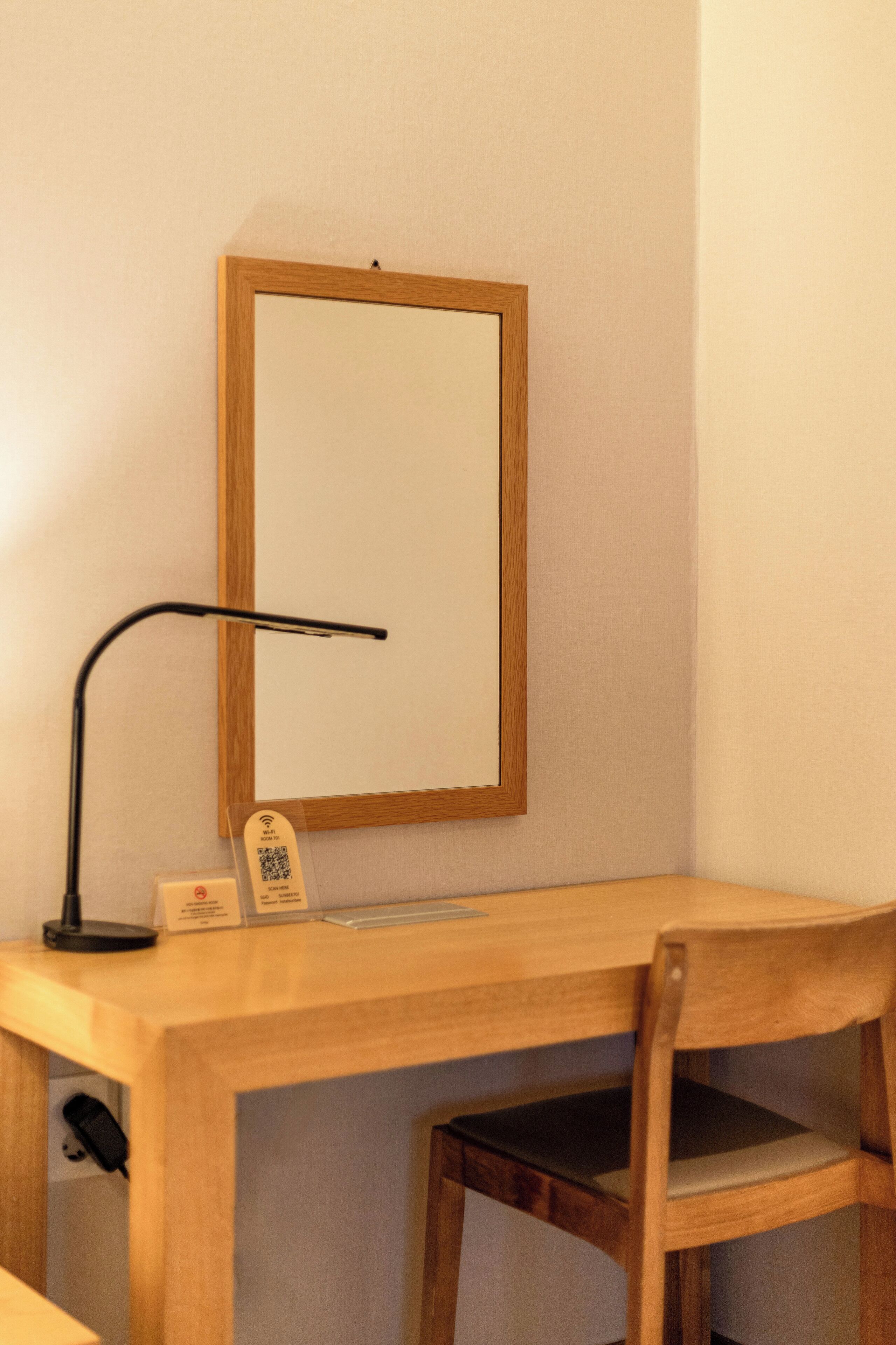 Un bureau en bois, une lampe de bureau noire, un miroir encadré et un panneau avec un code QR.