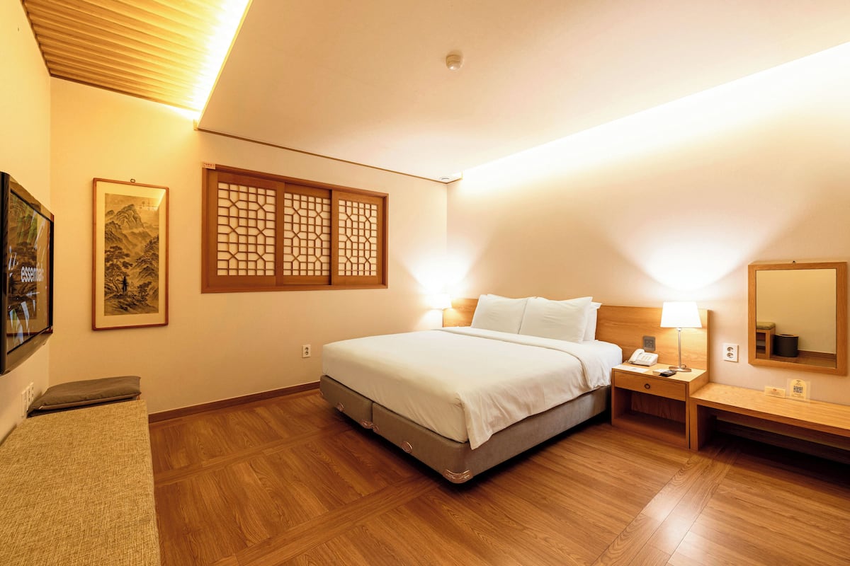 A hotel room with a bed, bedside tables, a nightstand, a wooden floor, a wall-mounted TV, and a traditional Japanese sliding door.