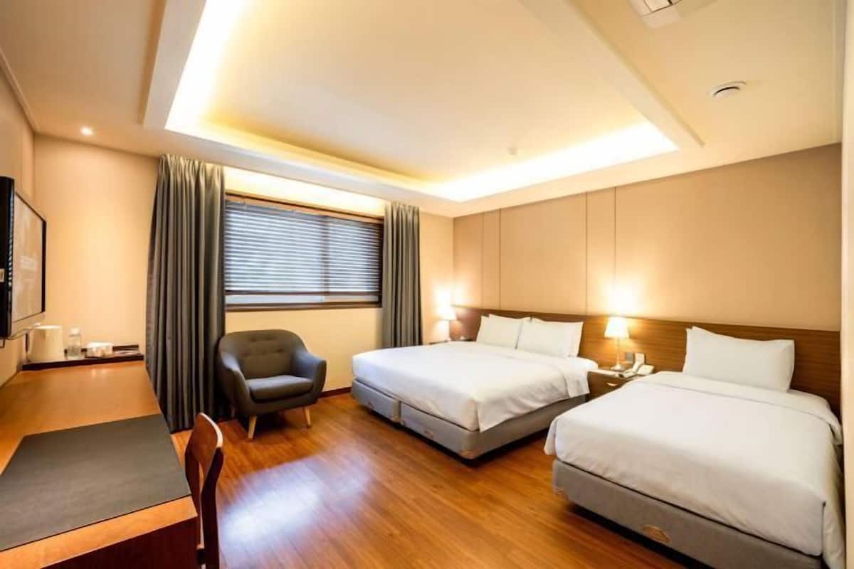 A hotel room with two beds, a desk, a chair, a TV, and a window with curtains.