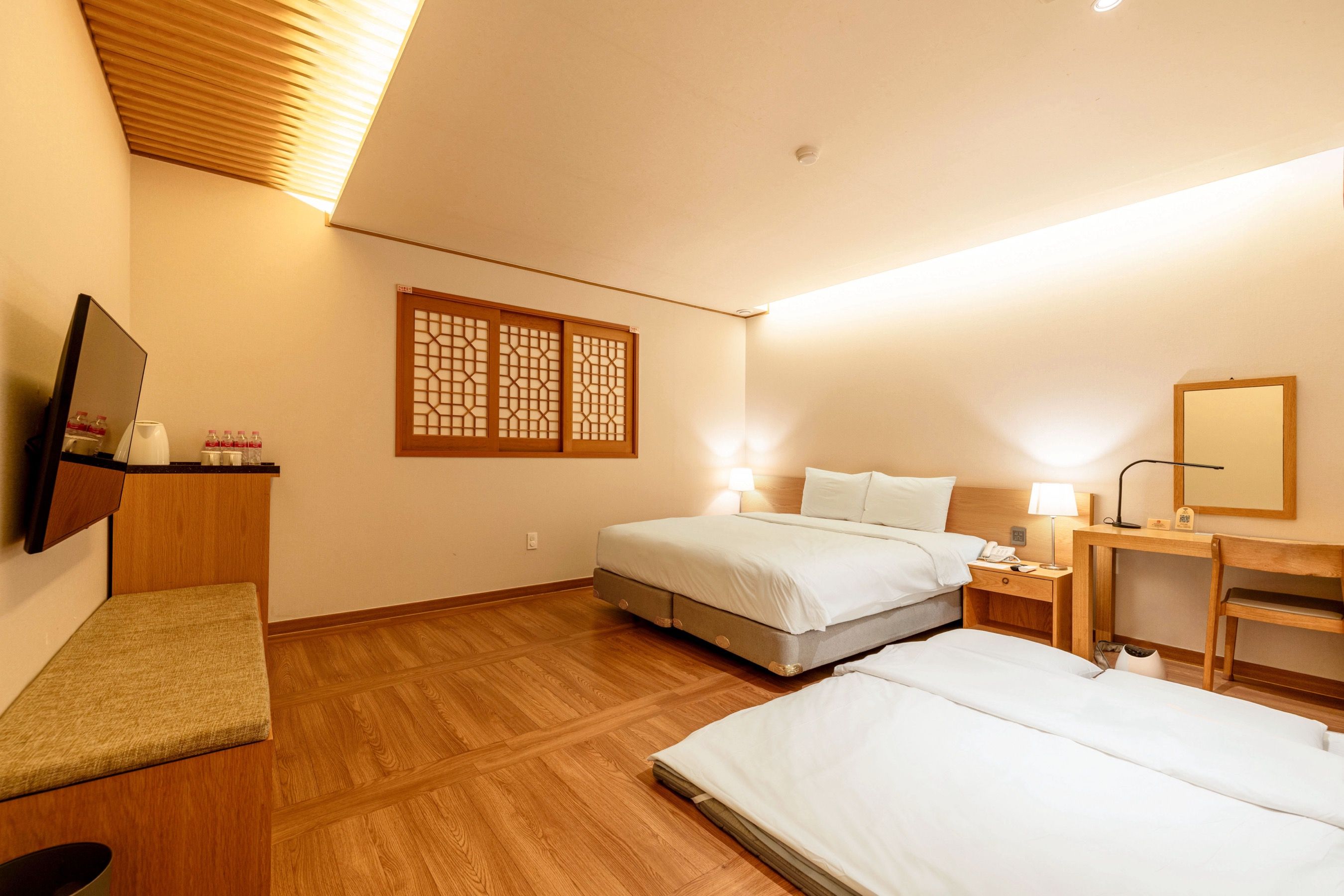 A hotel room with a bed, bedside table, lamp, and a TV mounted on the wall.