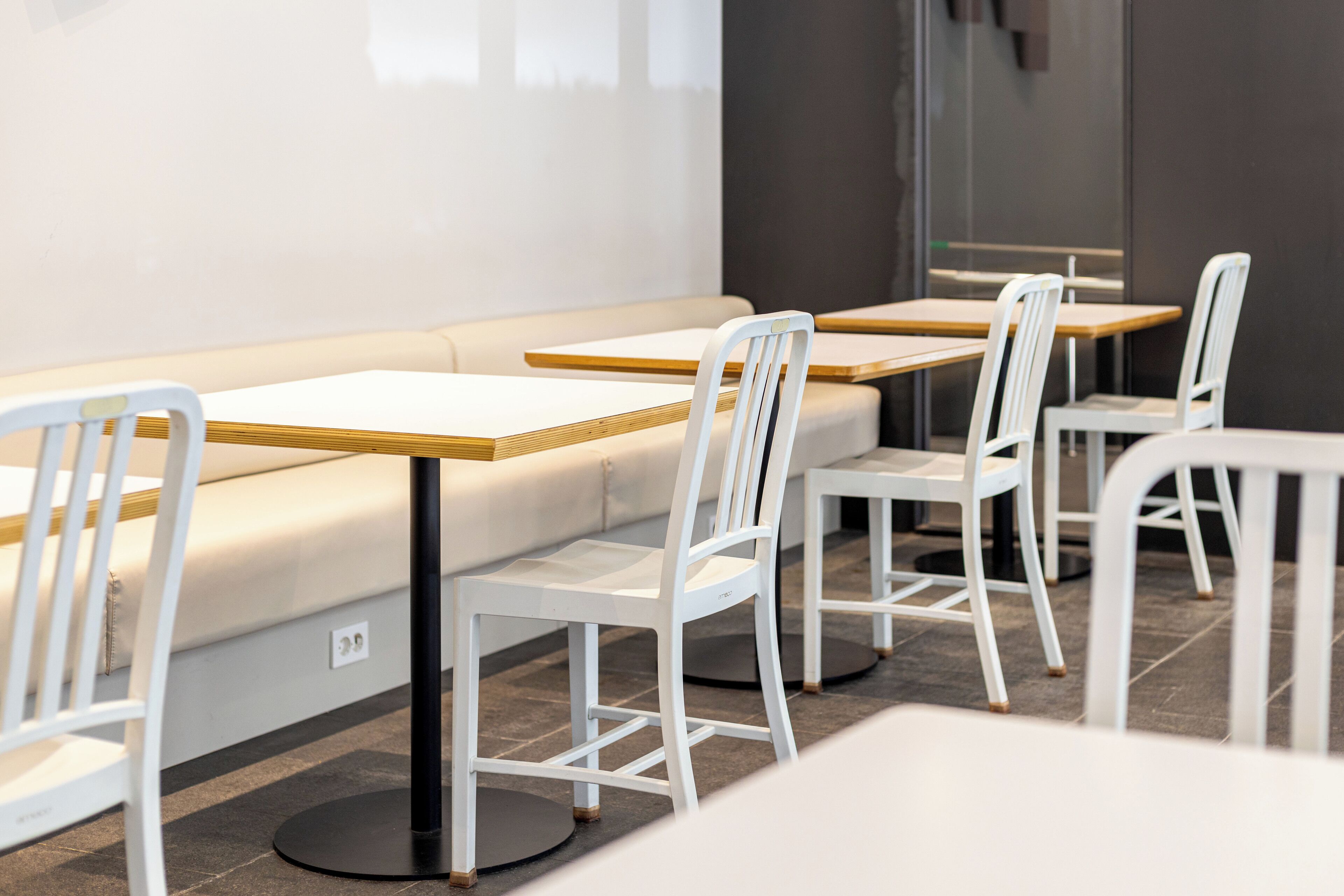 A modern dining area with white chairs and tables, a sofa, and a dark wall.