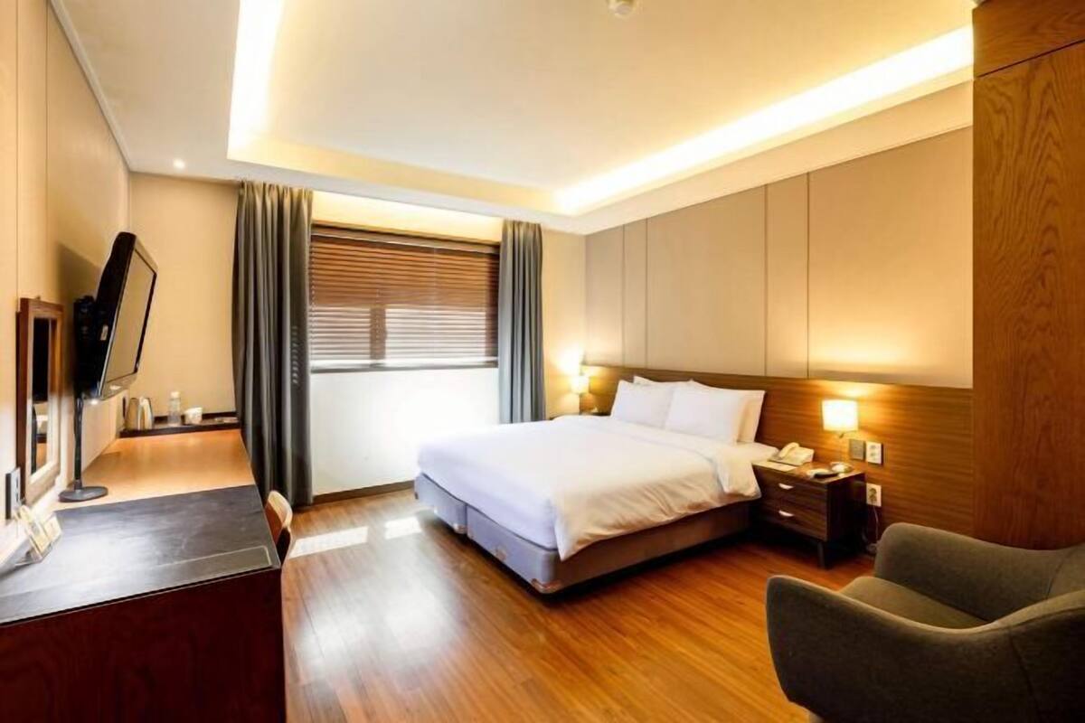 A hotel room with a bed, bedside table, lamp, and a TV on a desk.