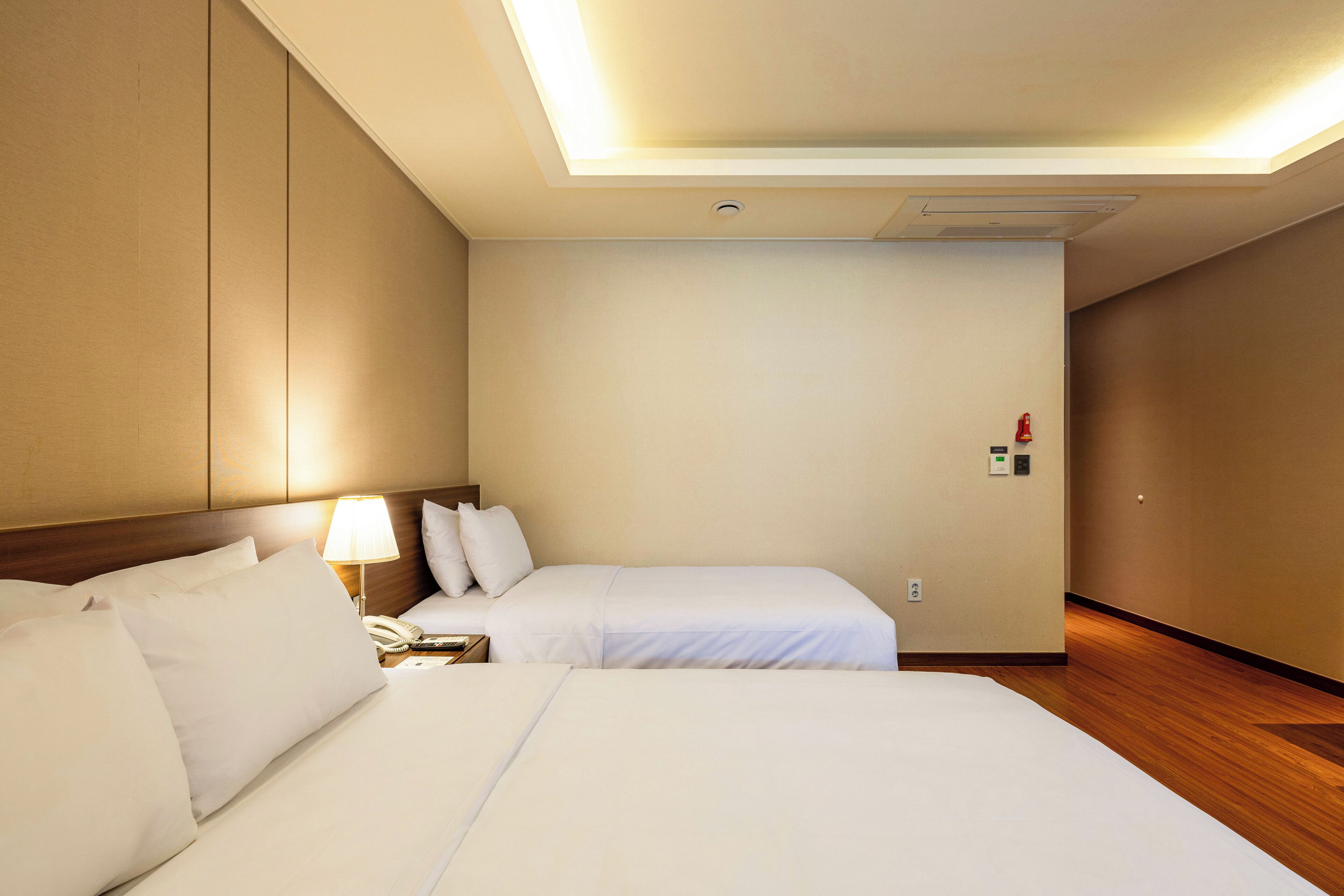 Une chambre d’hôtel avec deux lits, une table de chevet avec une lampe, un téléphone et un luminaire fixé au mur.
