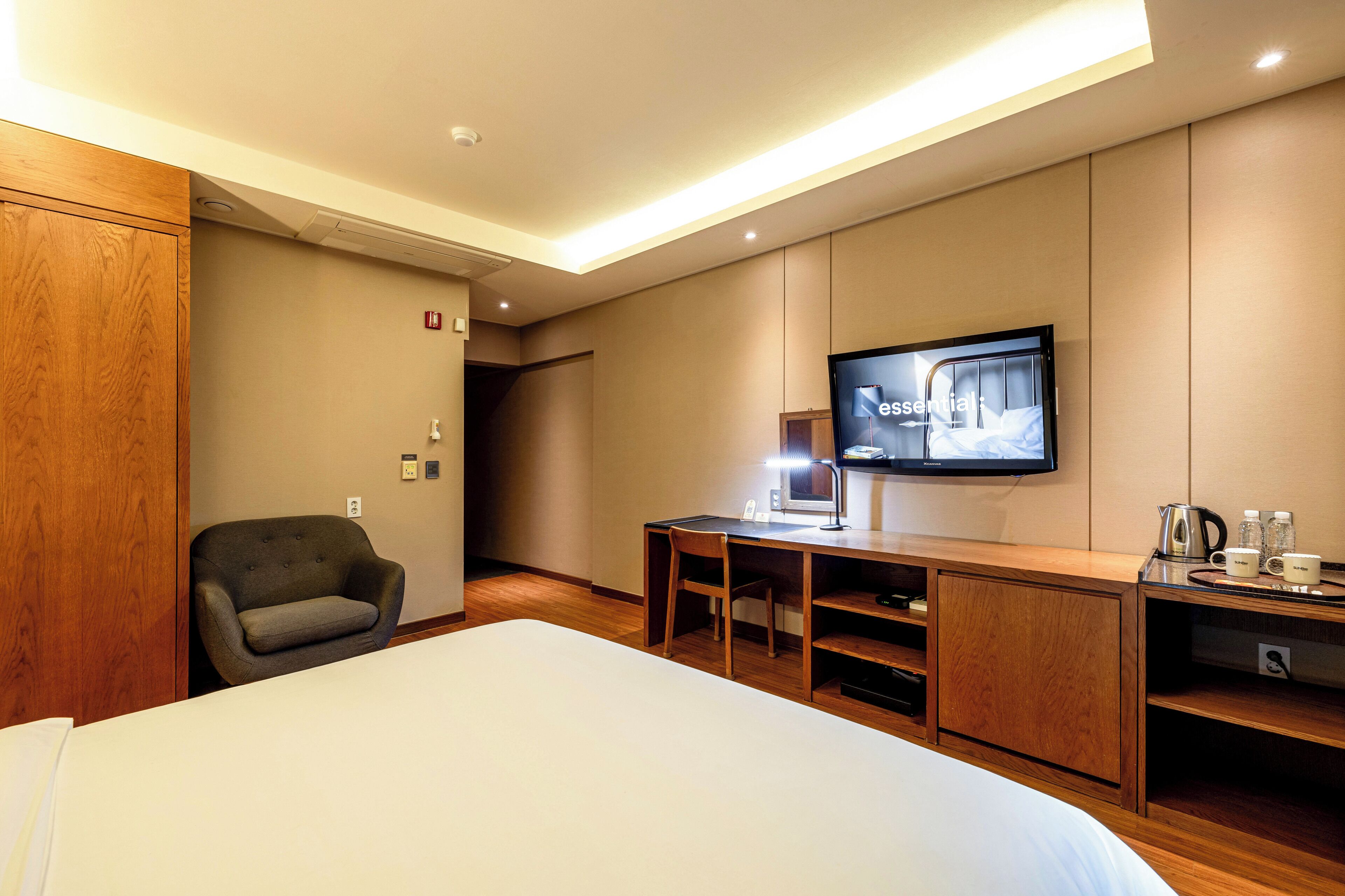 A hotel room with a large bed, a desk with a chair, a television, and a wooden wardrobe.