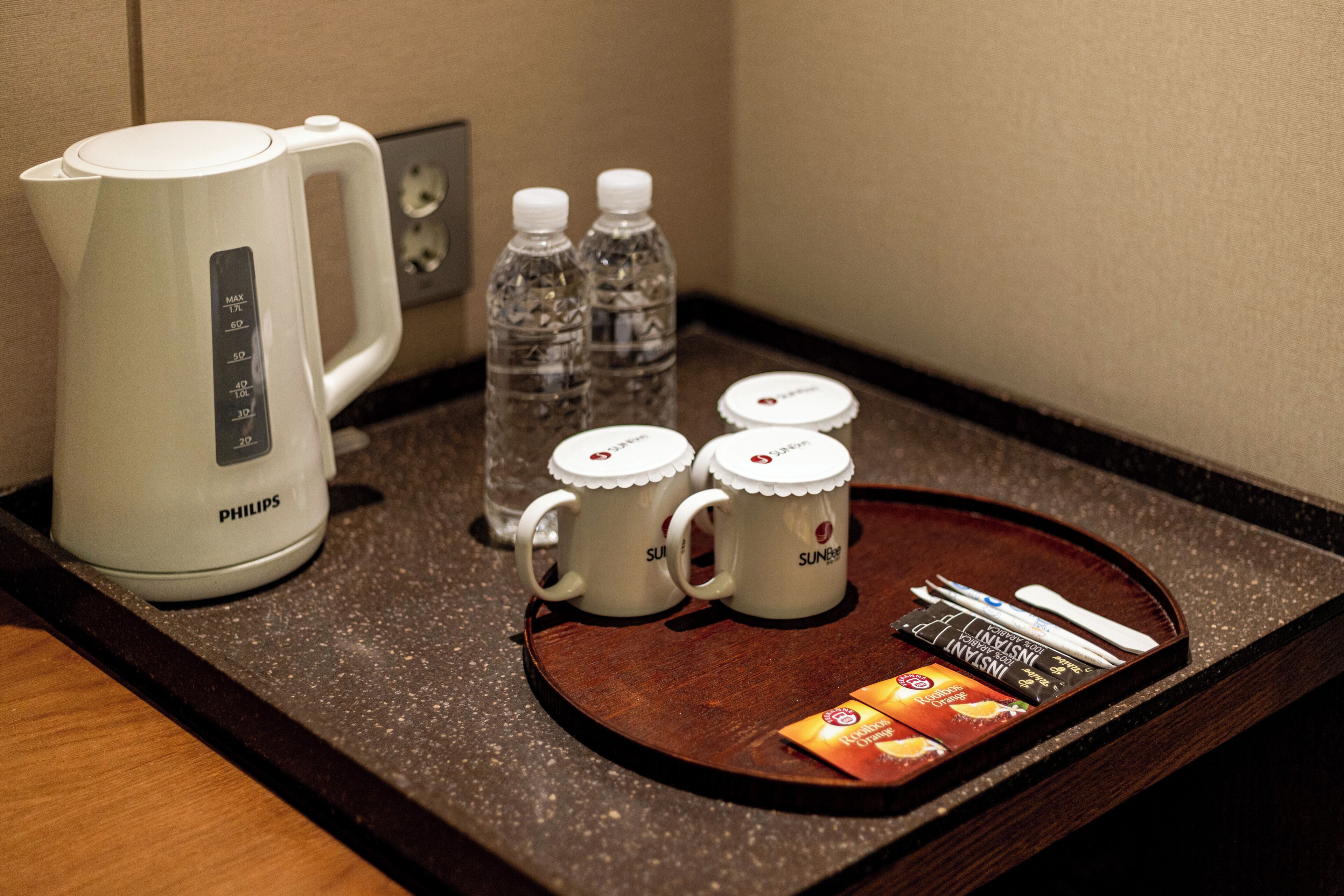 A hotel room's breakfast tray with a Philips coffee maker, two water bottles, two mugs, a tray of instant coffee packets, and a spoon.