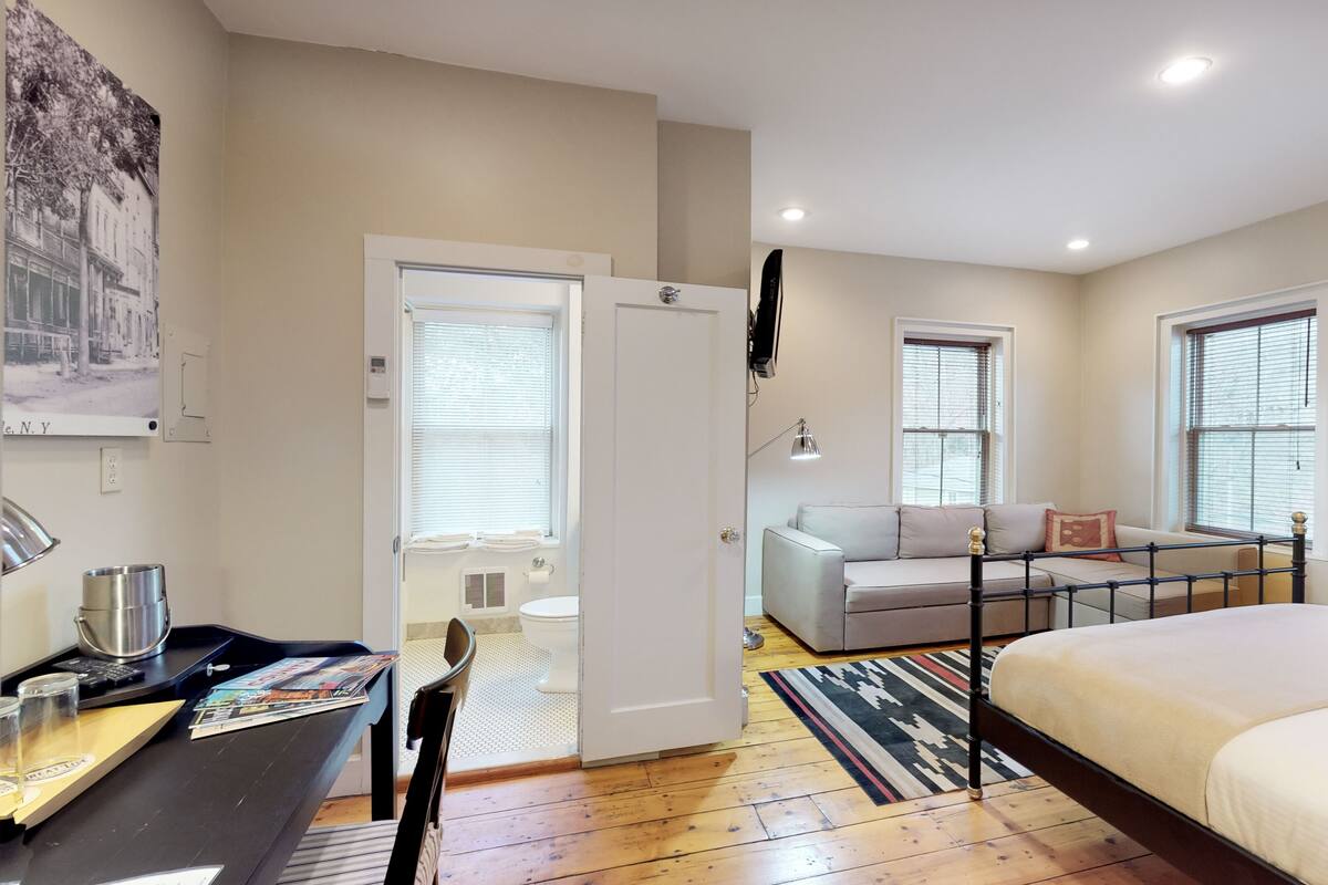 A bedroom with a bed, a desk with a chair, a sofa, and a window.