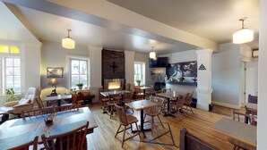 A spacious dining area with multiple wooden tables and chairs, a brick fireplace, and pendant lighting.