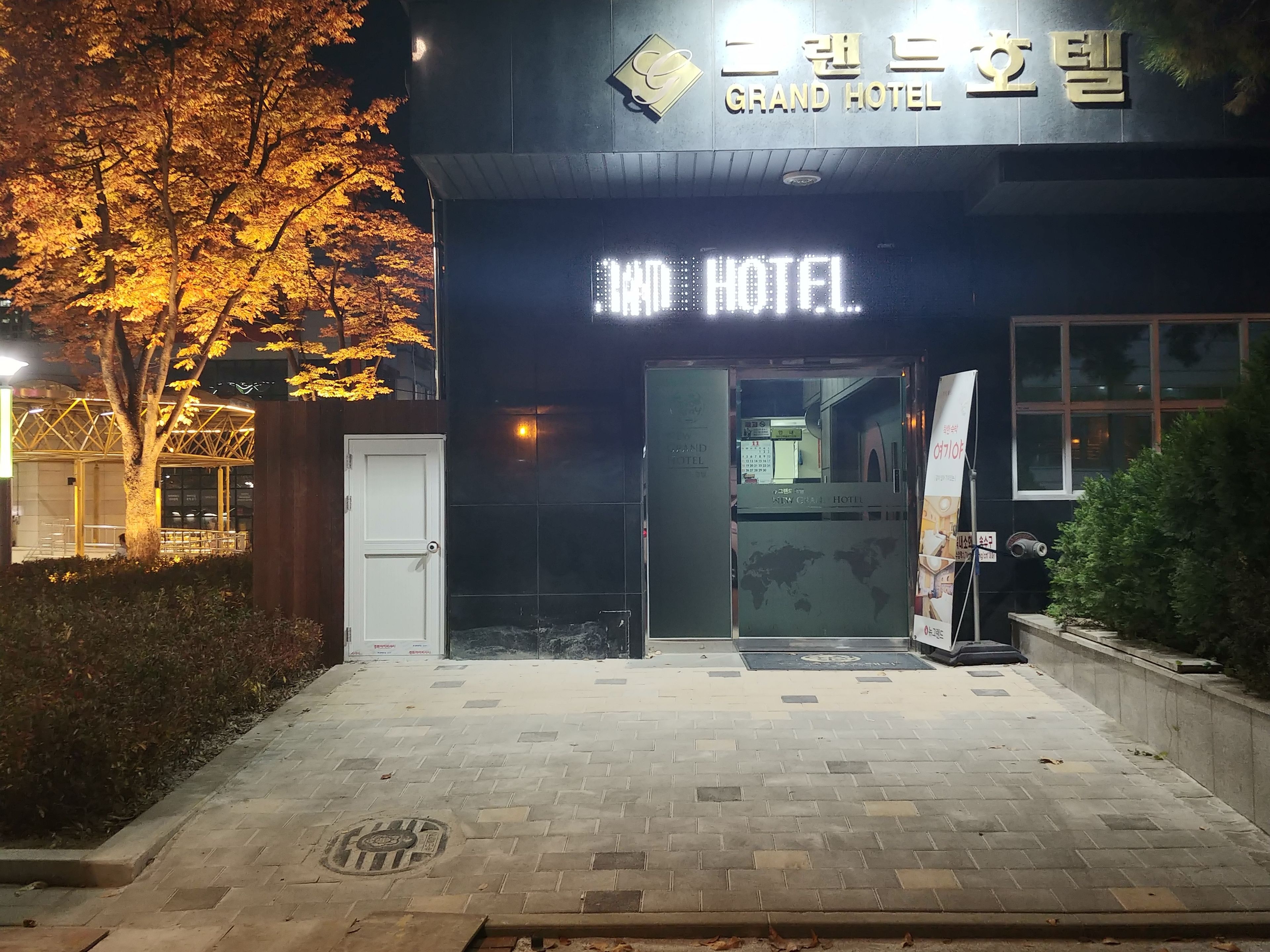 Grand Hotels facade med et markant, oplyst skilt, en lukket indgang og en belagt sti.