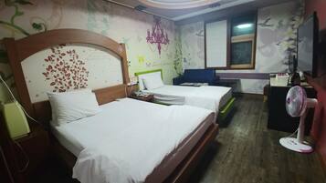A hotel room with two beds, a desk, a chair, a standing fan, and a window with blinds.