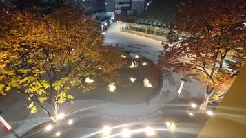 Vista nocturna de un paisaje urbano con árboles otoñales y una zona peatonal bien iluminada.