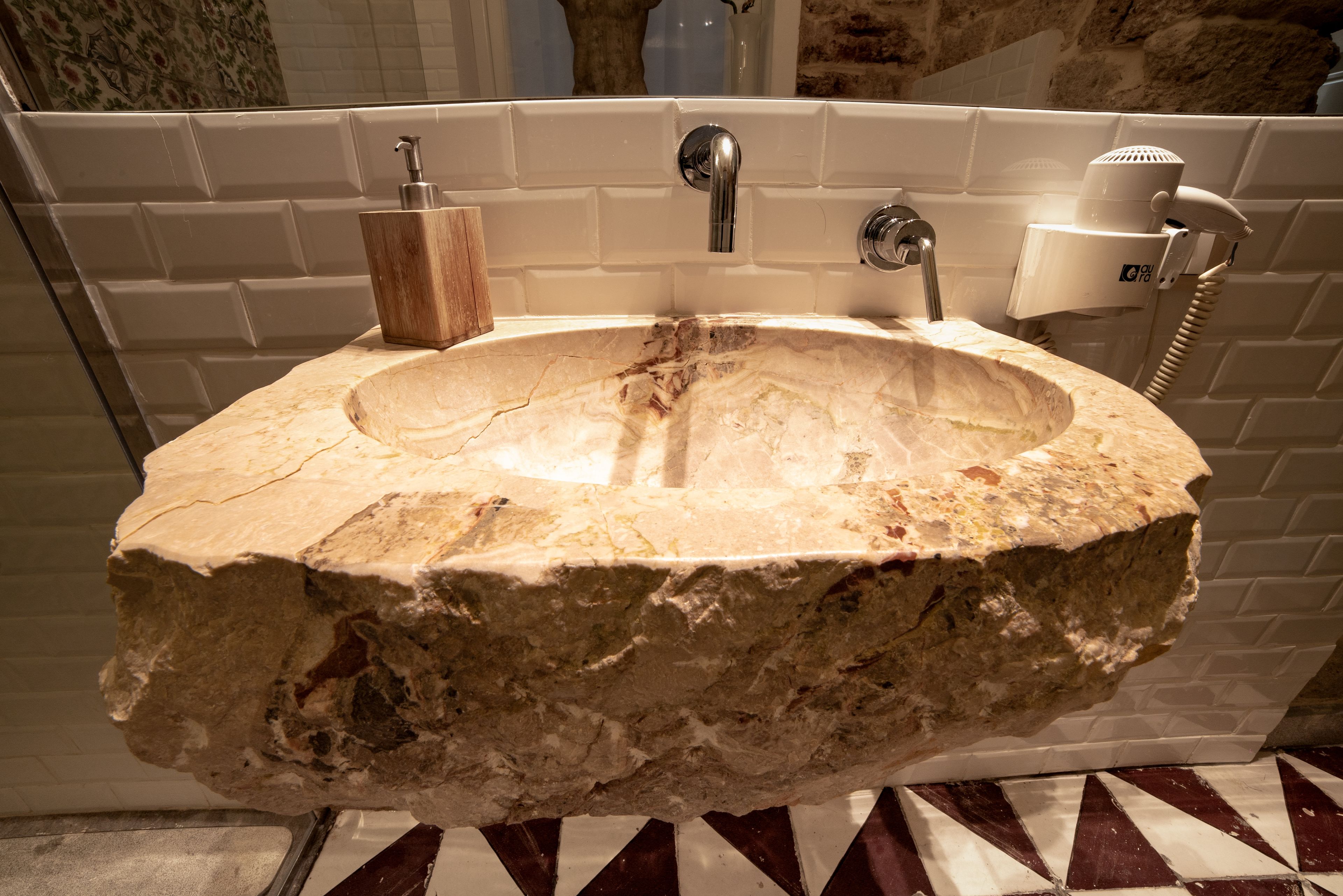 A bathroom with a large, irregularly shaped stone sink, a handheld showerhead, and a bottle of soap.