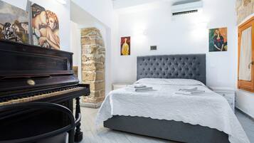 Un dormitorio con un piano, una cama con cabecera gris y obras de arte en las paredes.