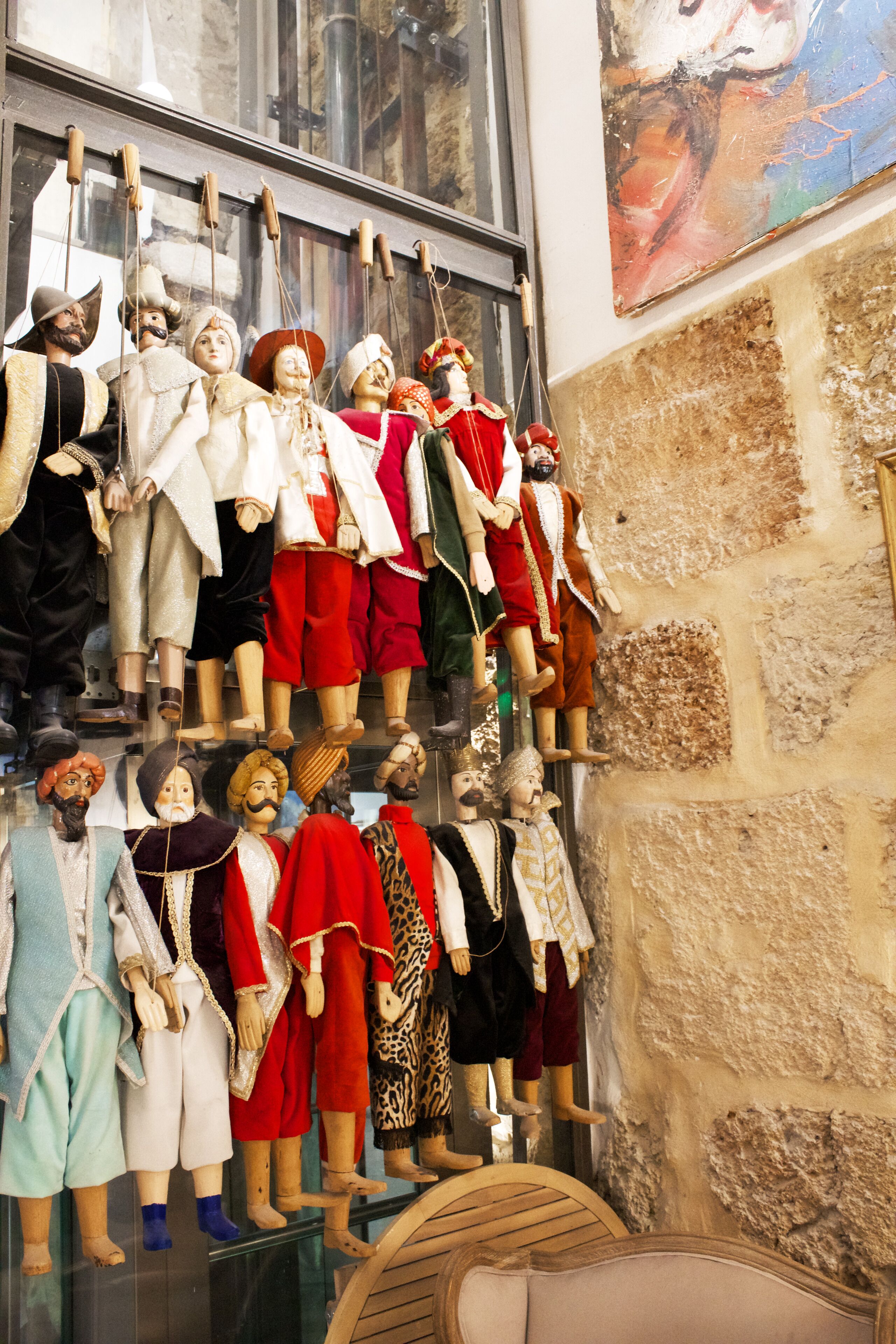 Una colección de figuras de madera con diversos atuendos exhibida en estanterías frente a un muro de piedra.