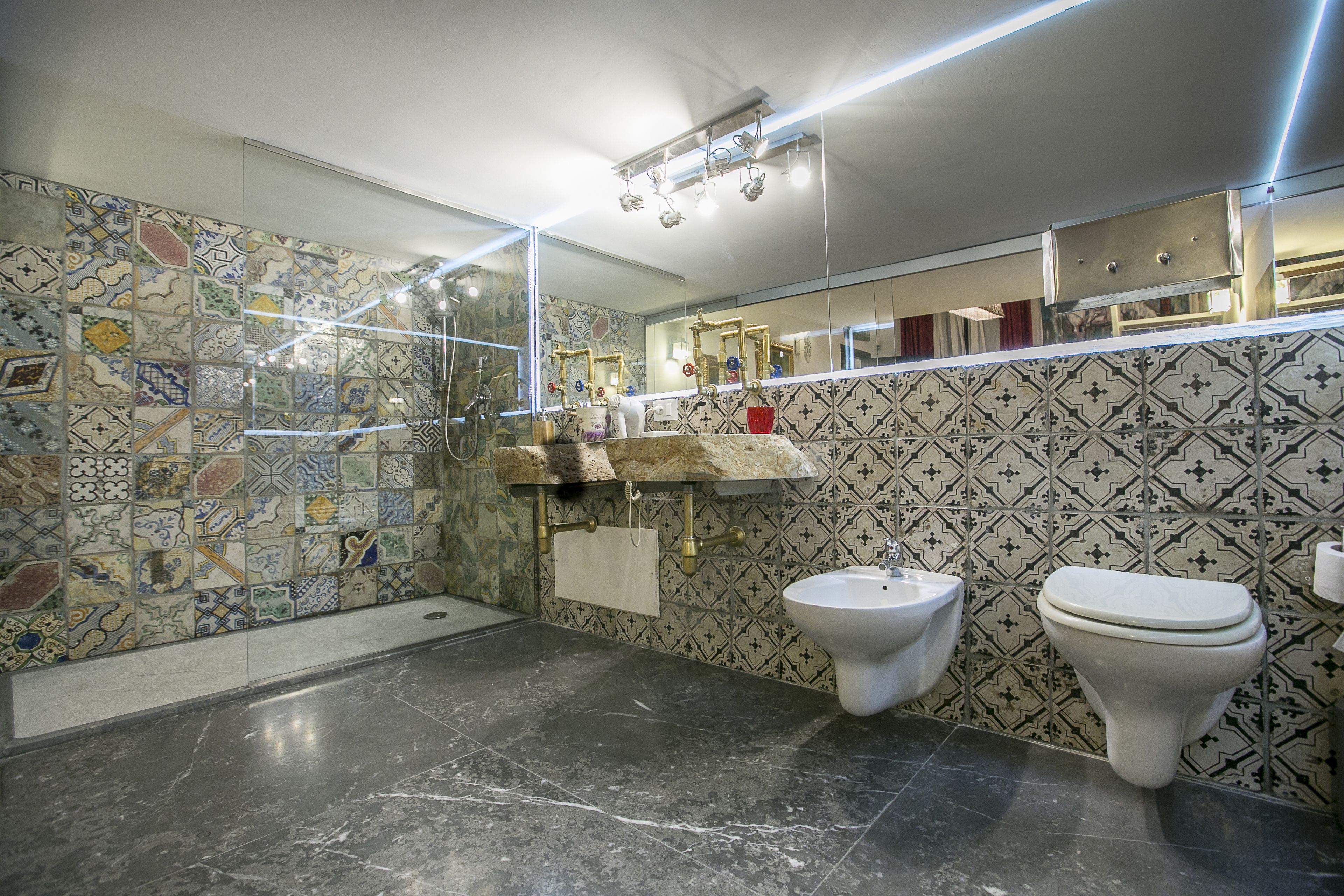 A bathroom with a tiled wall, a marble floor, a sink, a bidet, and a mirror.