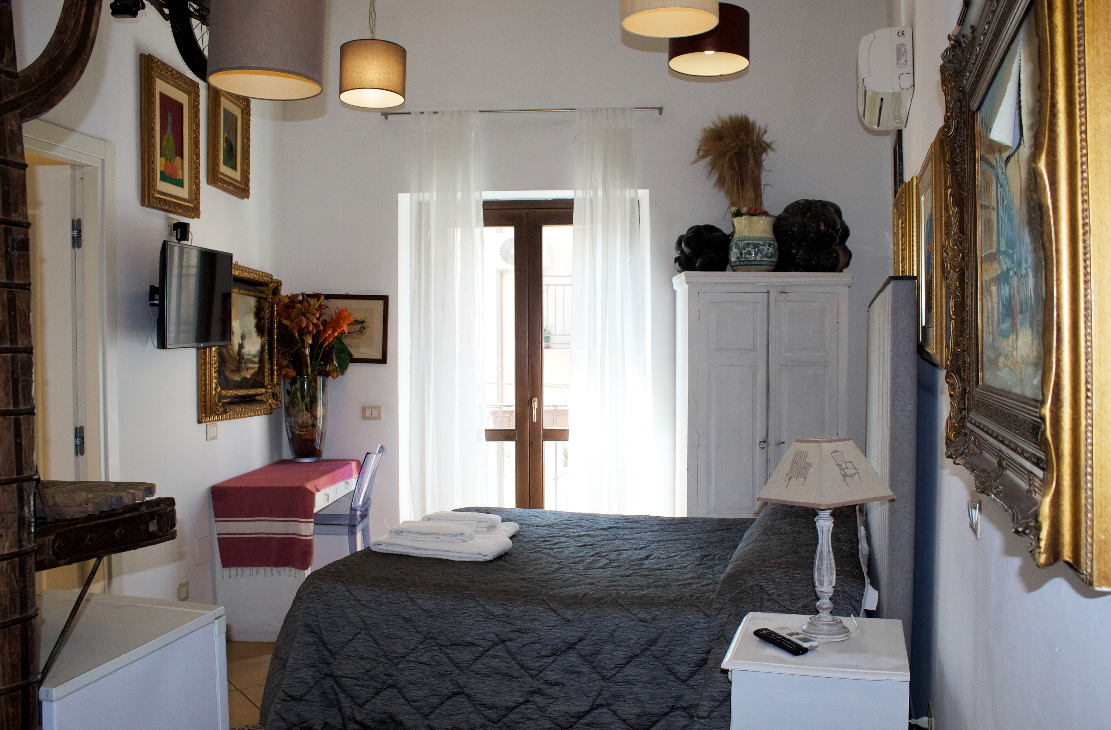 Une chambre à coucher comprenant un lit, une télévision, une lampe, une commode et une porte donnant sur un balcon.