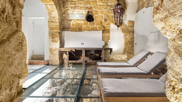 Una habitación con paredes de piedra y techo de madera, un banco y dos sillones.