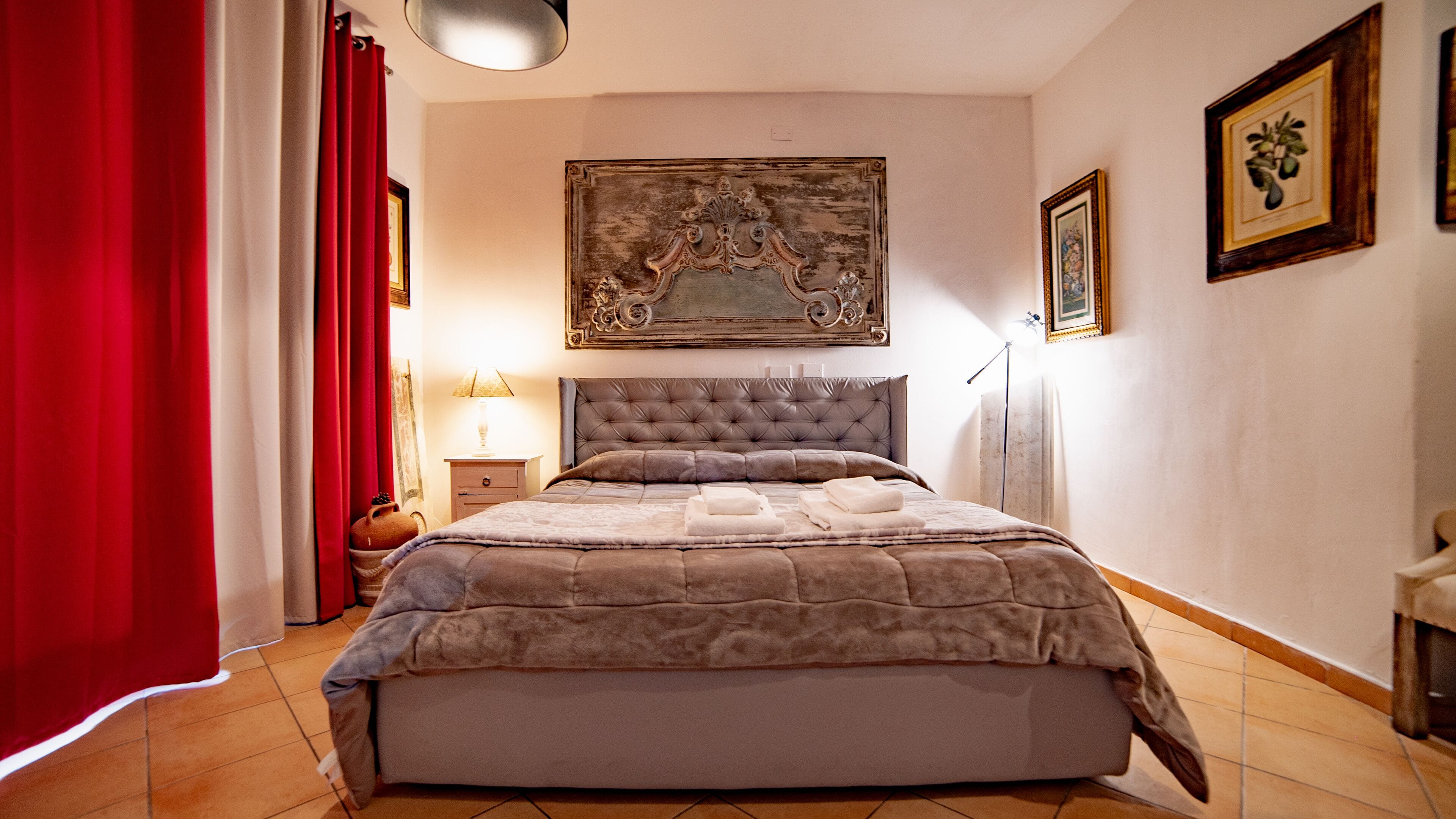 A bedroom with a tufted headboard, a large painting above the bed, and a red curtain on the left.