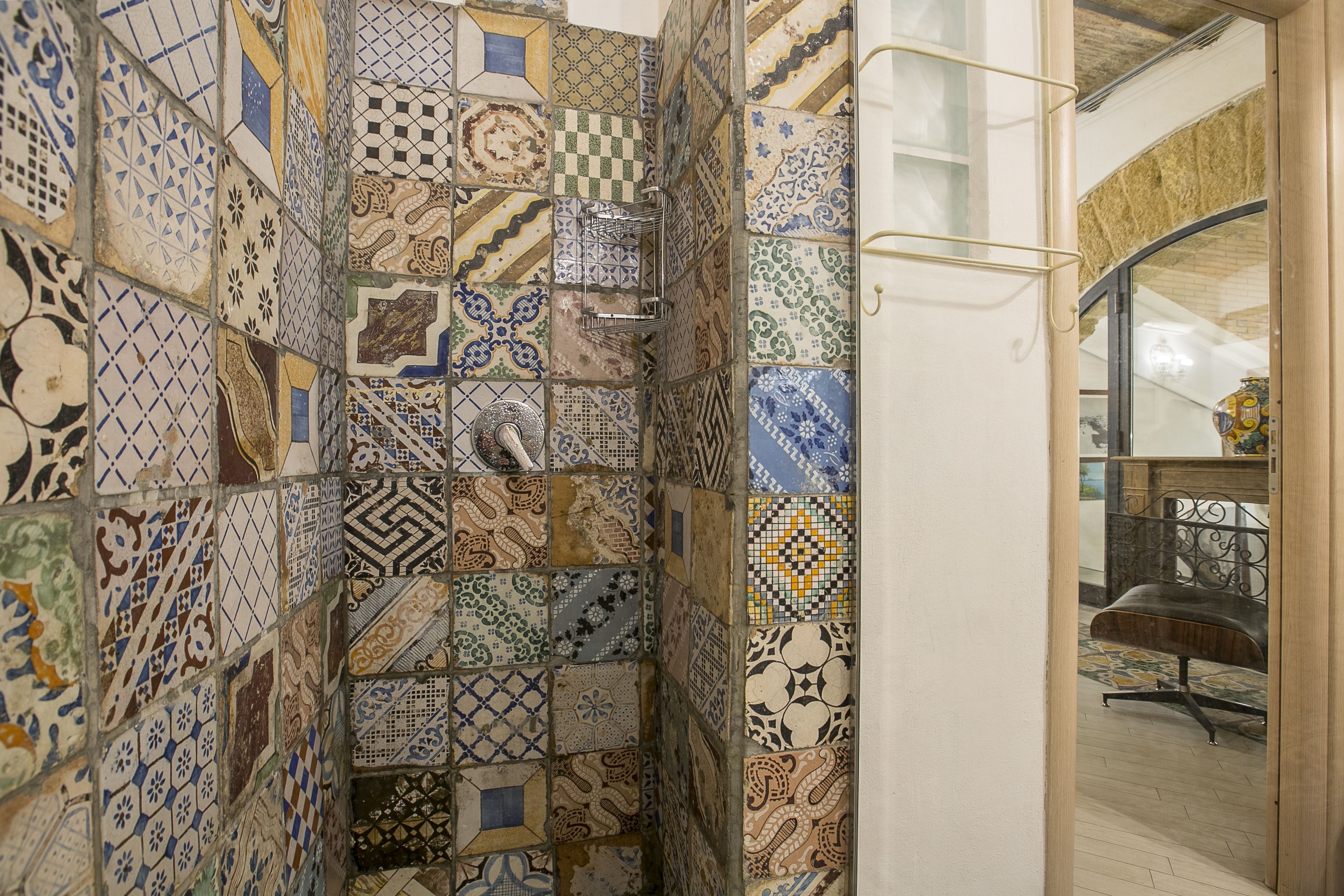 Una habitación con diversos azulejos decorativos en las paredes, una silla de metal y una puerta de cristal que da a otra zona.