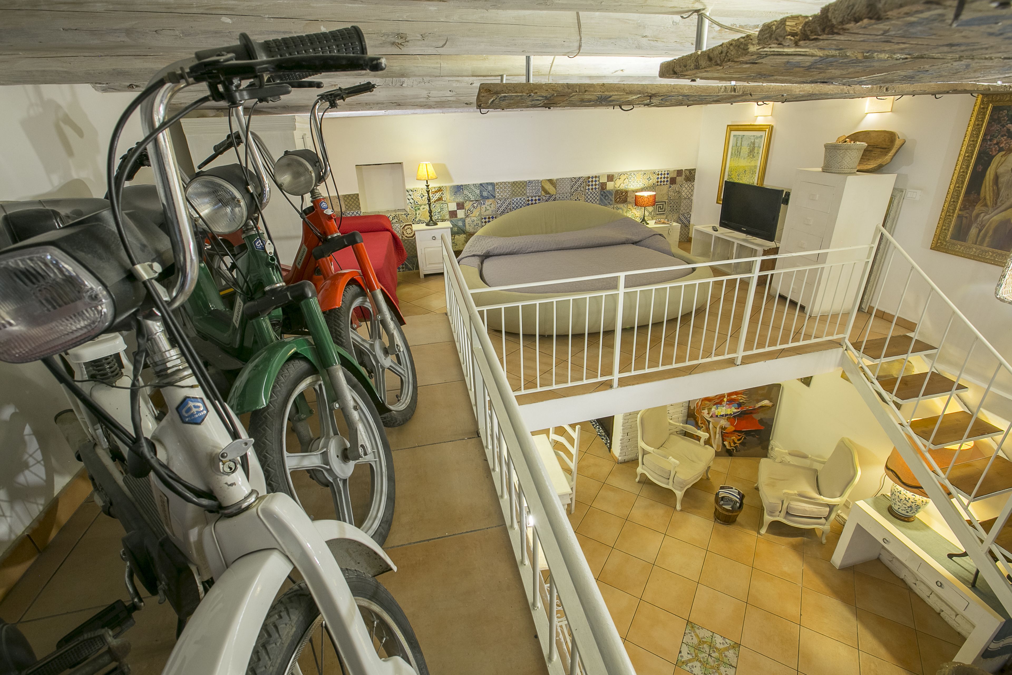 A multi-level room with a bed, a desk, and a chair. There are two motorcycles parked against the wall.