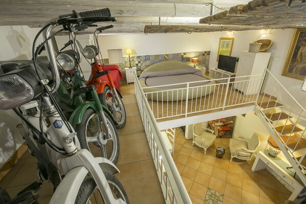 A multi-level room with a bed, a desk, and a chair. There are two motorcycles parked against the wall.