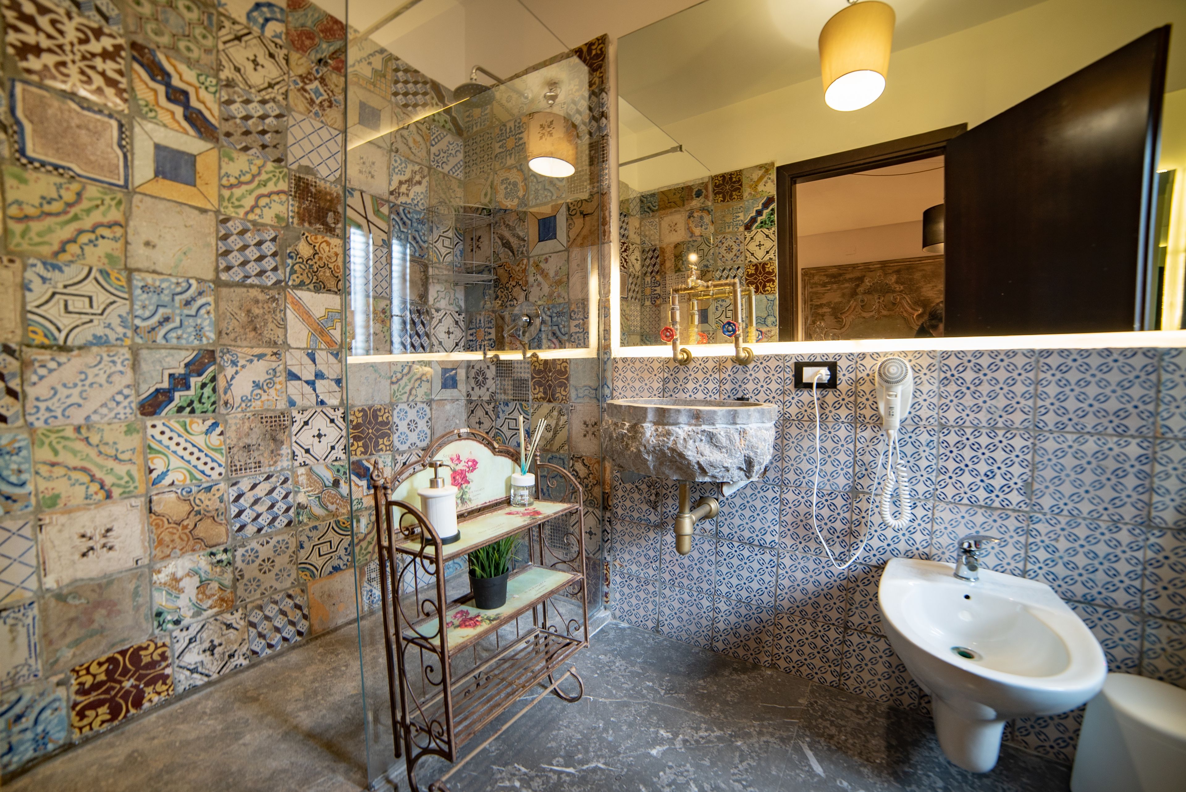 A bathroom with a tiled wall, a sink, a bidet, and a shelf with toiletries.