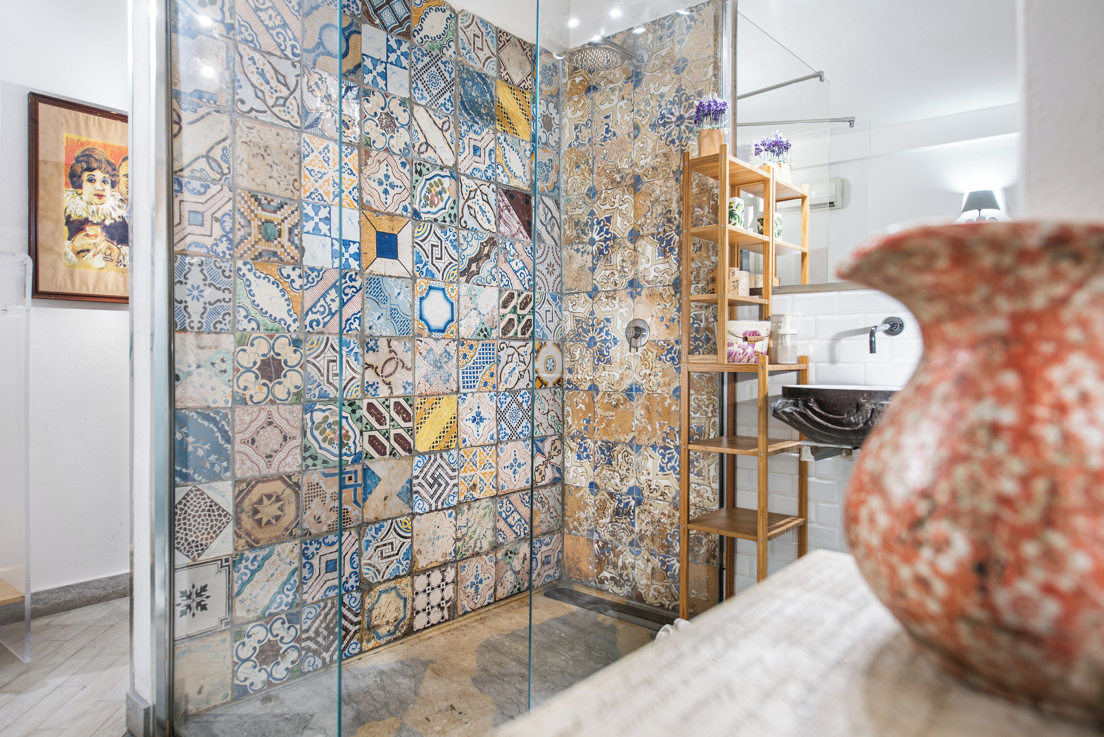 Une salle de bain avec une douche carrelée, une étagère en bois où sont rangés les articles de toilette et une œuvre d’art encadrée au mur.