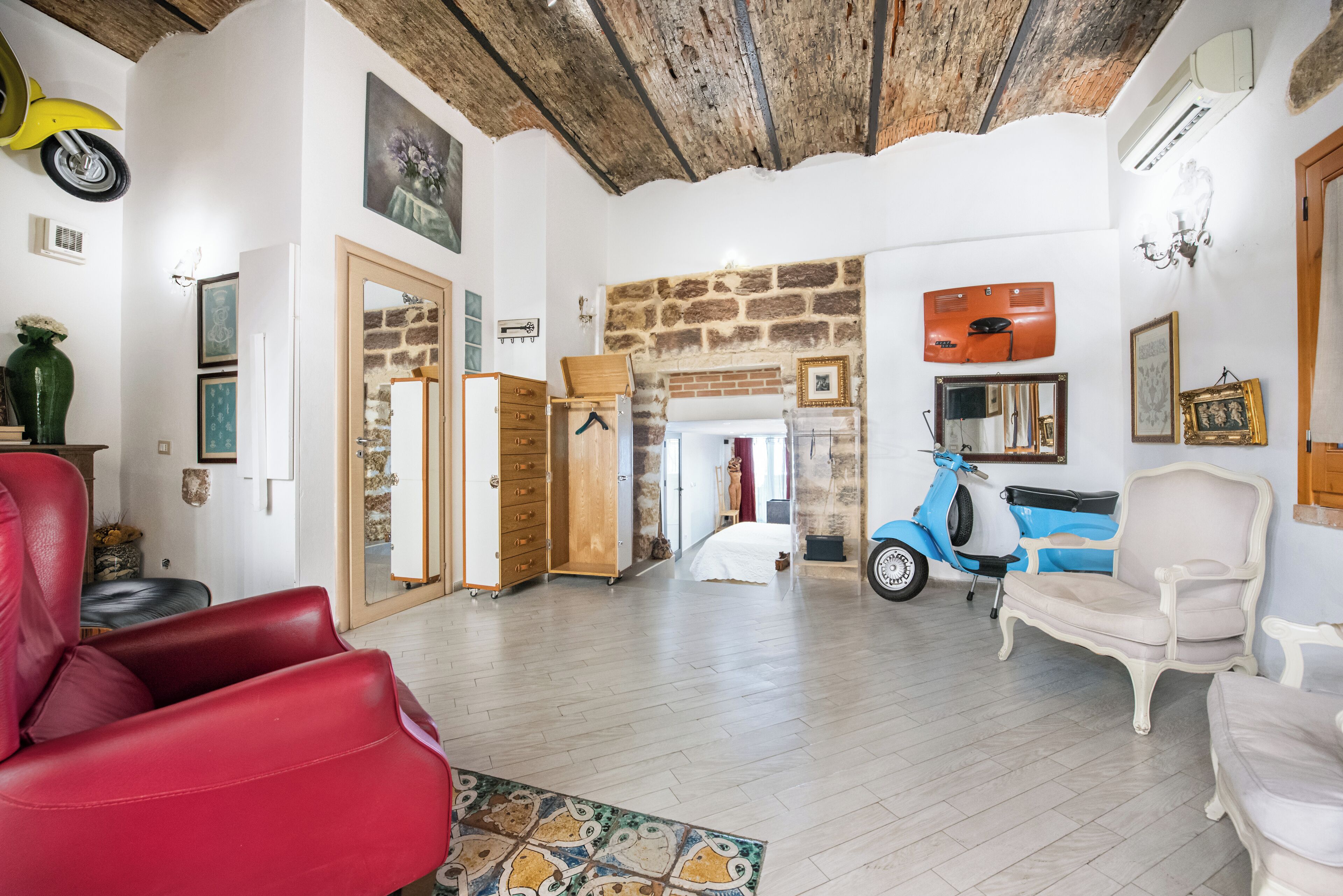 Un vaste espace de vie comprenant un fauteuil en cuir rouge, une trottinette bleue et un fauteuil blanc.