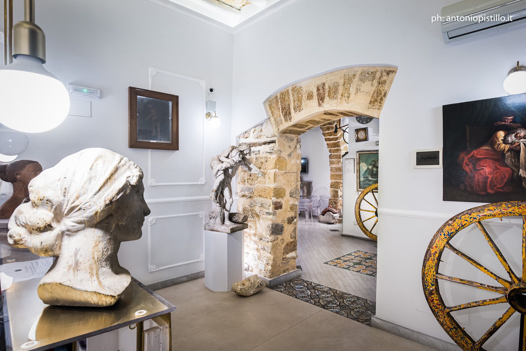 Un interior con un arco de piedra, un busto y una rueda grande y ornamentada.