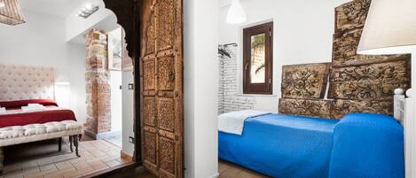 A bedroom with a large wooden door, a bed with a red and white headboard, and a blue bedspread.
