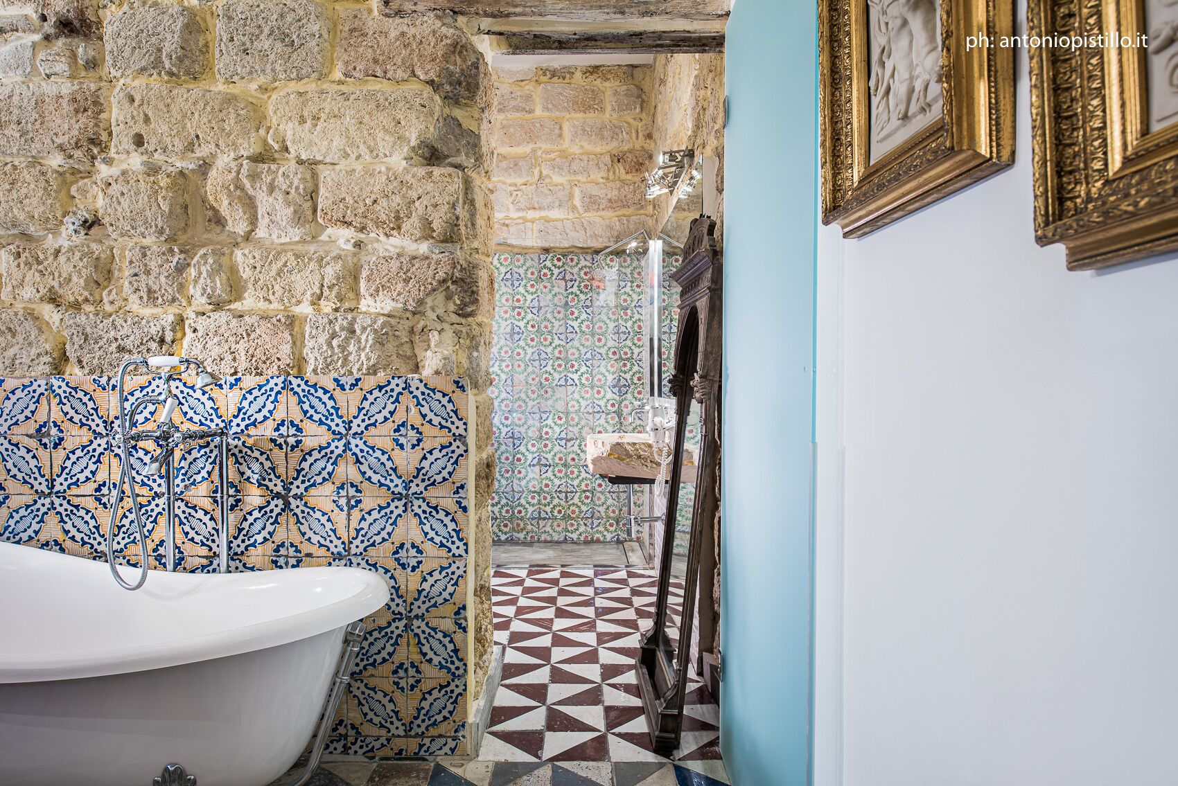 A bathroom with a stone wall, a white bathtub, patterned tiles, and a tiled floor.