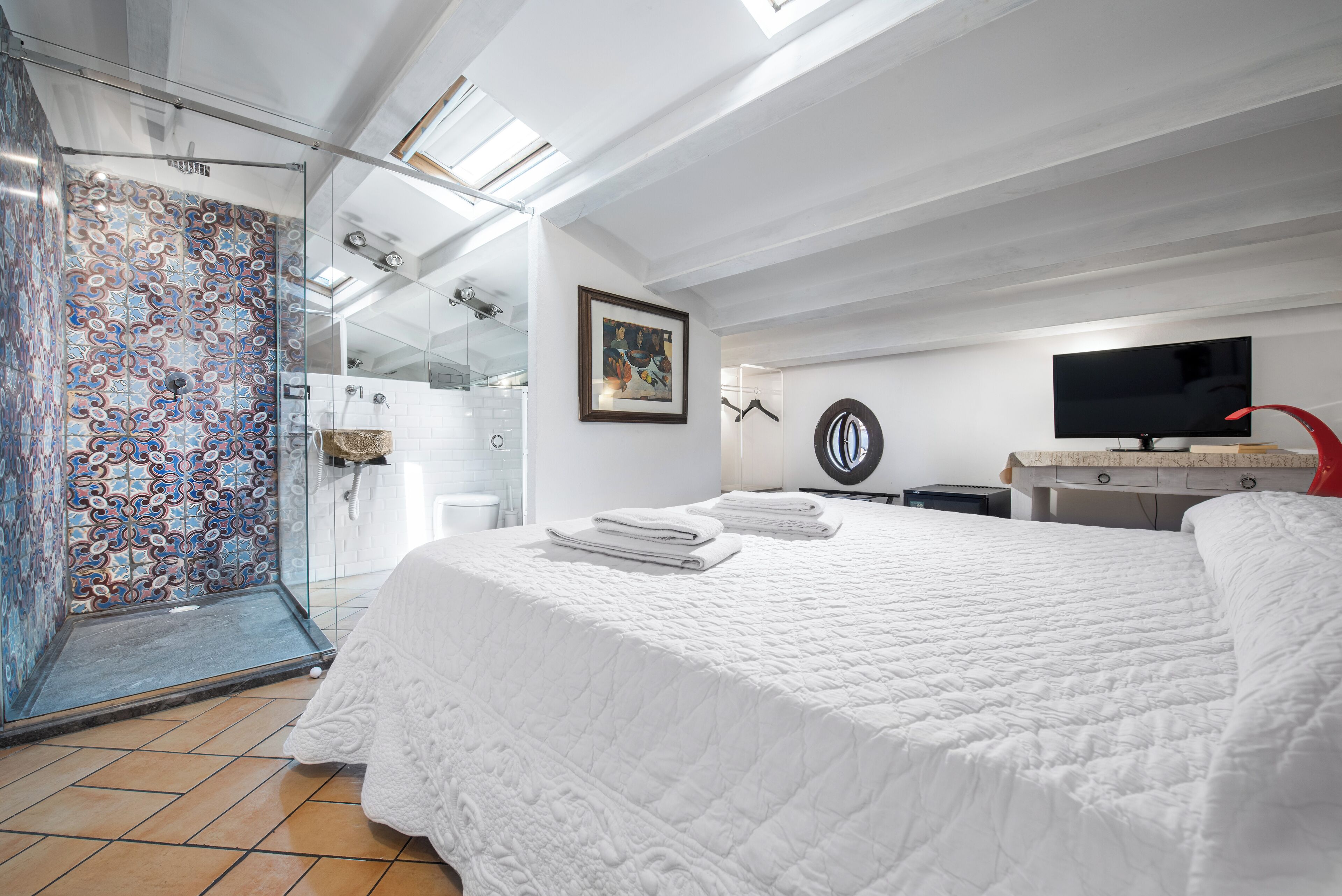 Una habitación de hotel moderna con una cama grande, una ducha con puerta de vidrio, un televisor de pantalla plana y un cuadro en la pared.