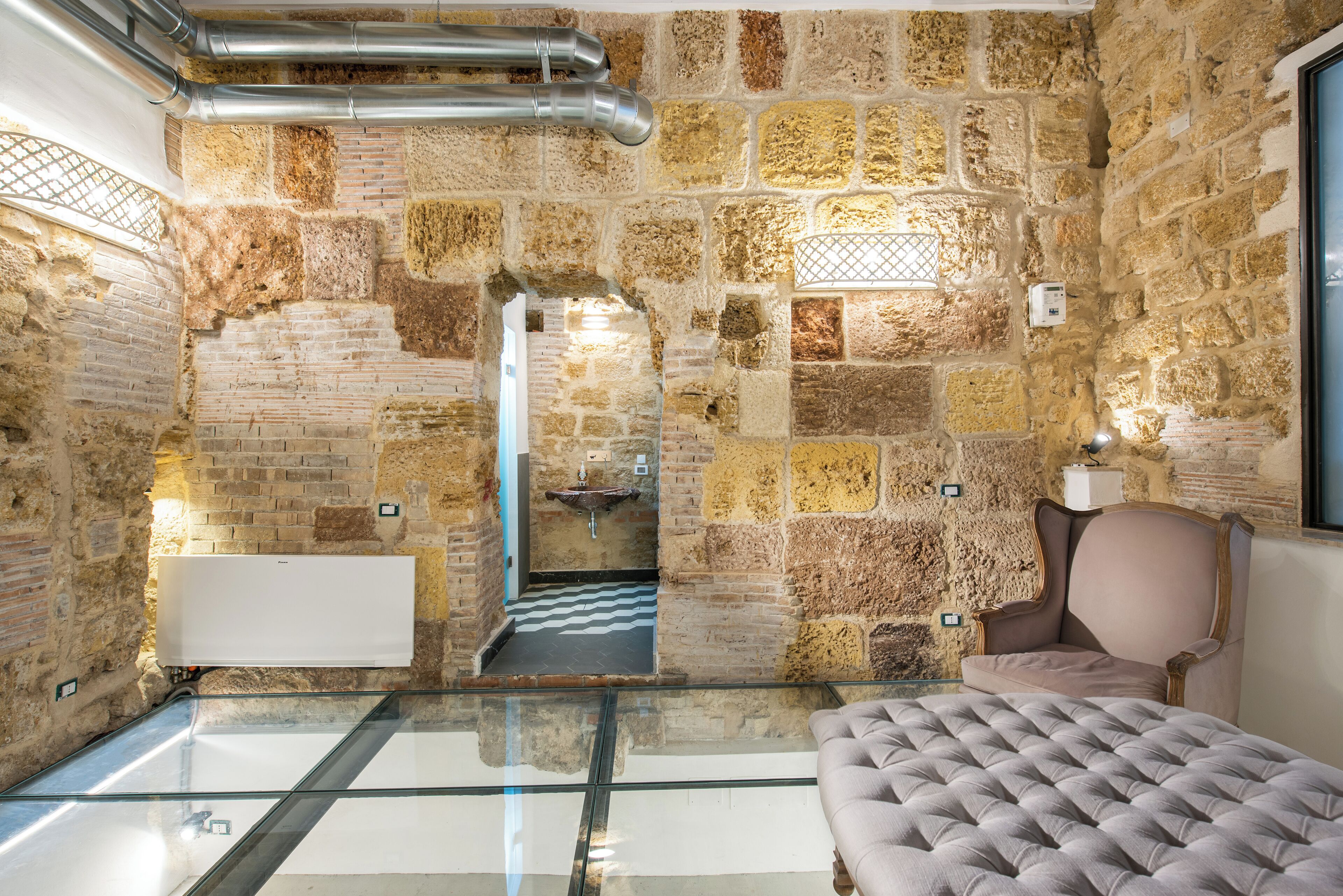 A room with stone walls, a glass floor, a bed, and a chair.