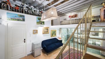 Une pièce avec un canapé bleu, un escalier et un plafond avec des poutres apparentes.
