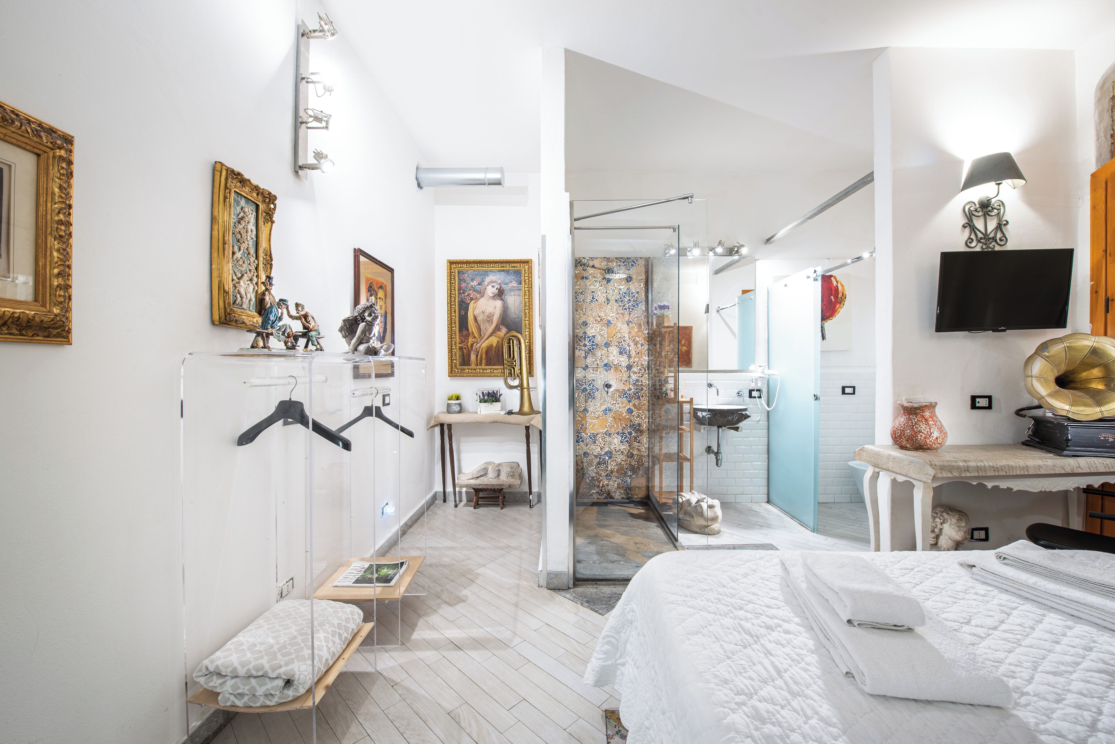 A modern hotel room with a bed, a desk, a vanity, and a shower area.