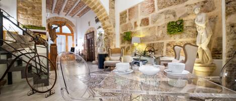 A room with a clear glass table set for tea, stone walls, and a statue.
