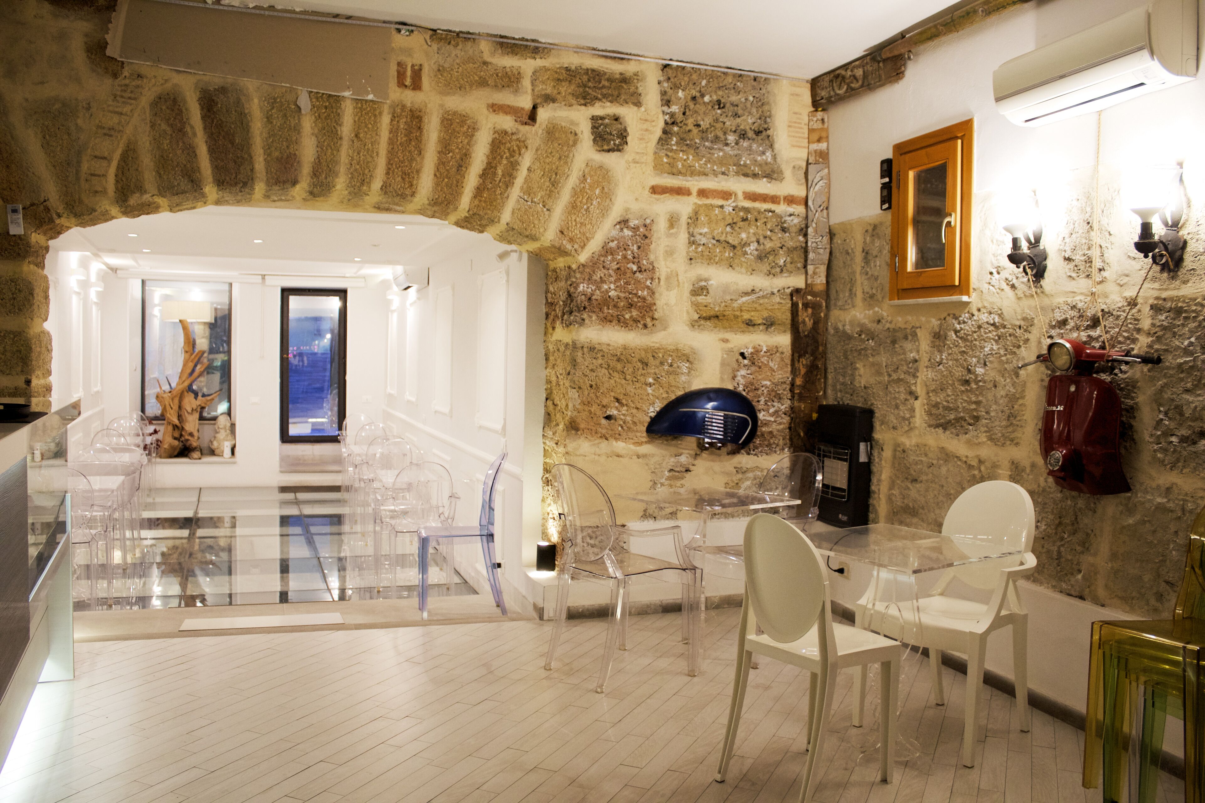 A modern interior with a stone wall, a glass table, and clear plastic chairs.