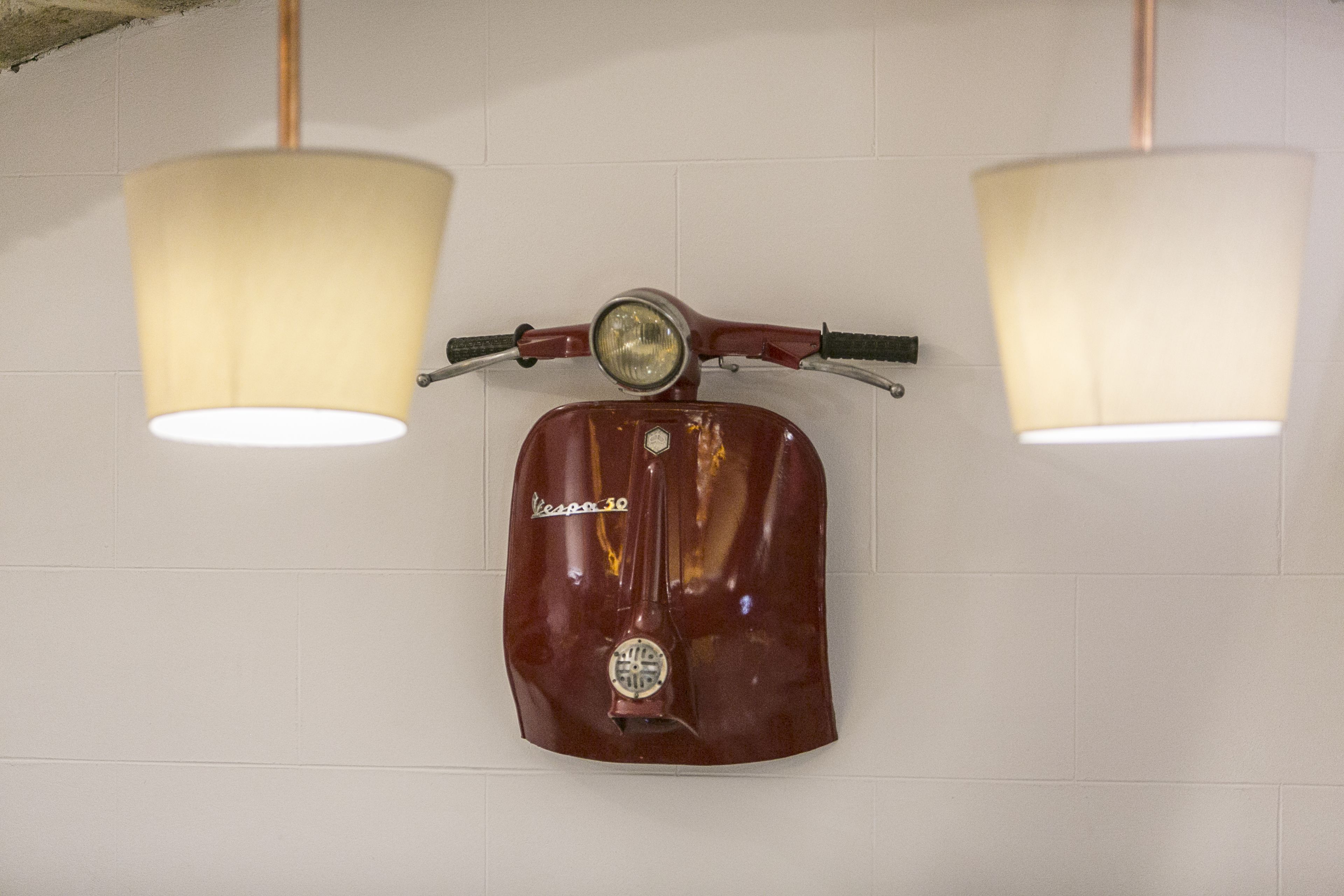Una Vespa 50 antigua montada en una pared con dos lámparas colgantes.