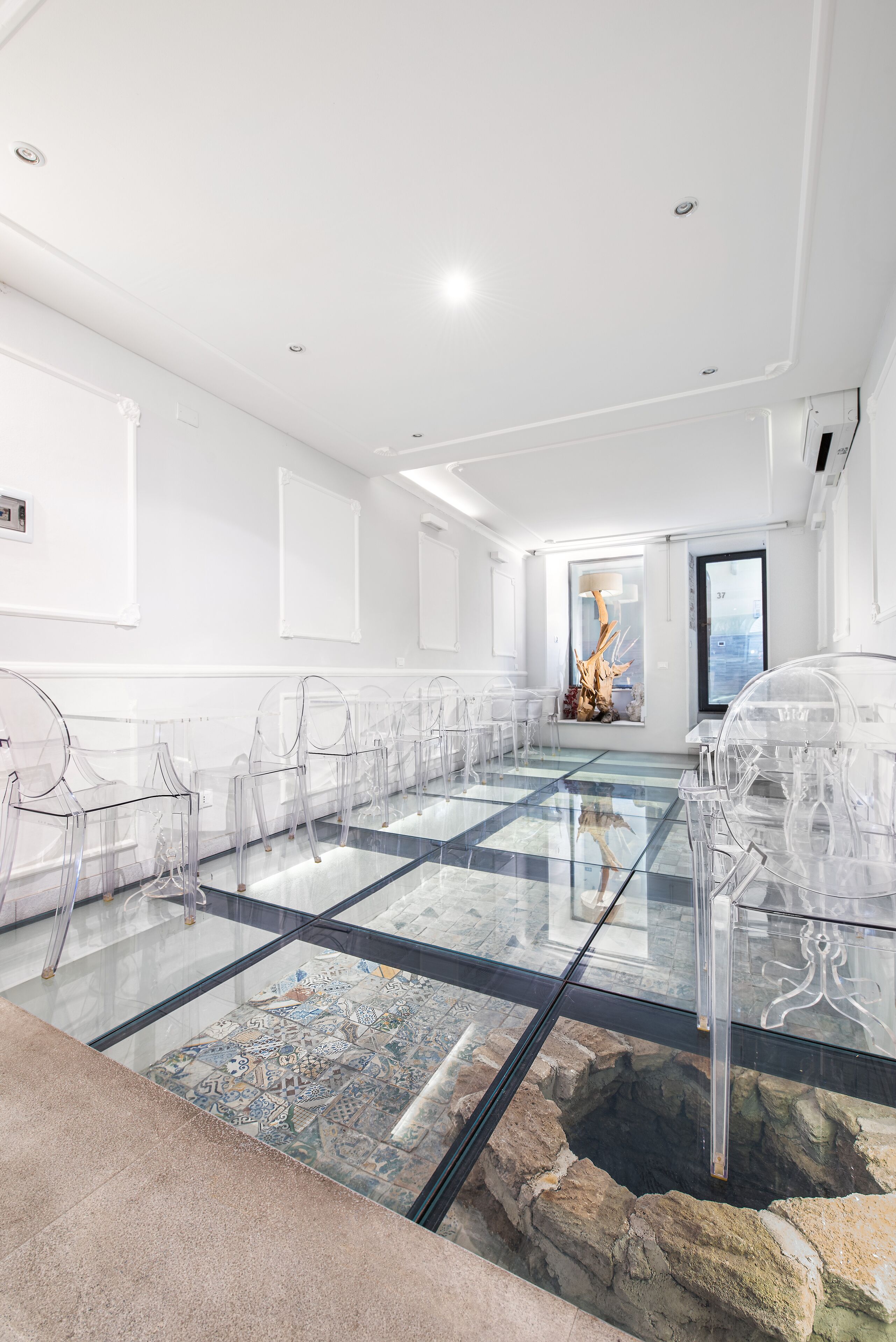 A modern conference room with glass tables and chairs, a patterned floor, and a stone wall feature.