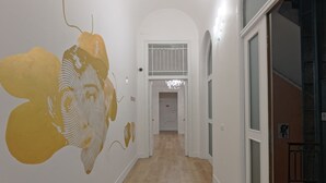 A hallway with white walls and a wooden floor, leading to a door with a metal gate. - Afea Art & Rooms (Palermo)
