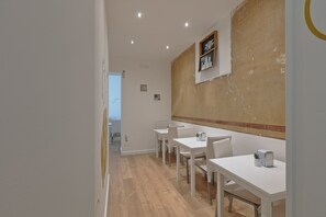 A modern dining area with white tables and chairs, a wooden floor, and a wall with a decorative element. - Afea Art & Rooms (Palermo)