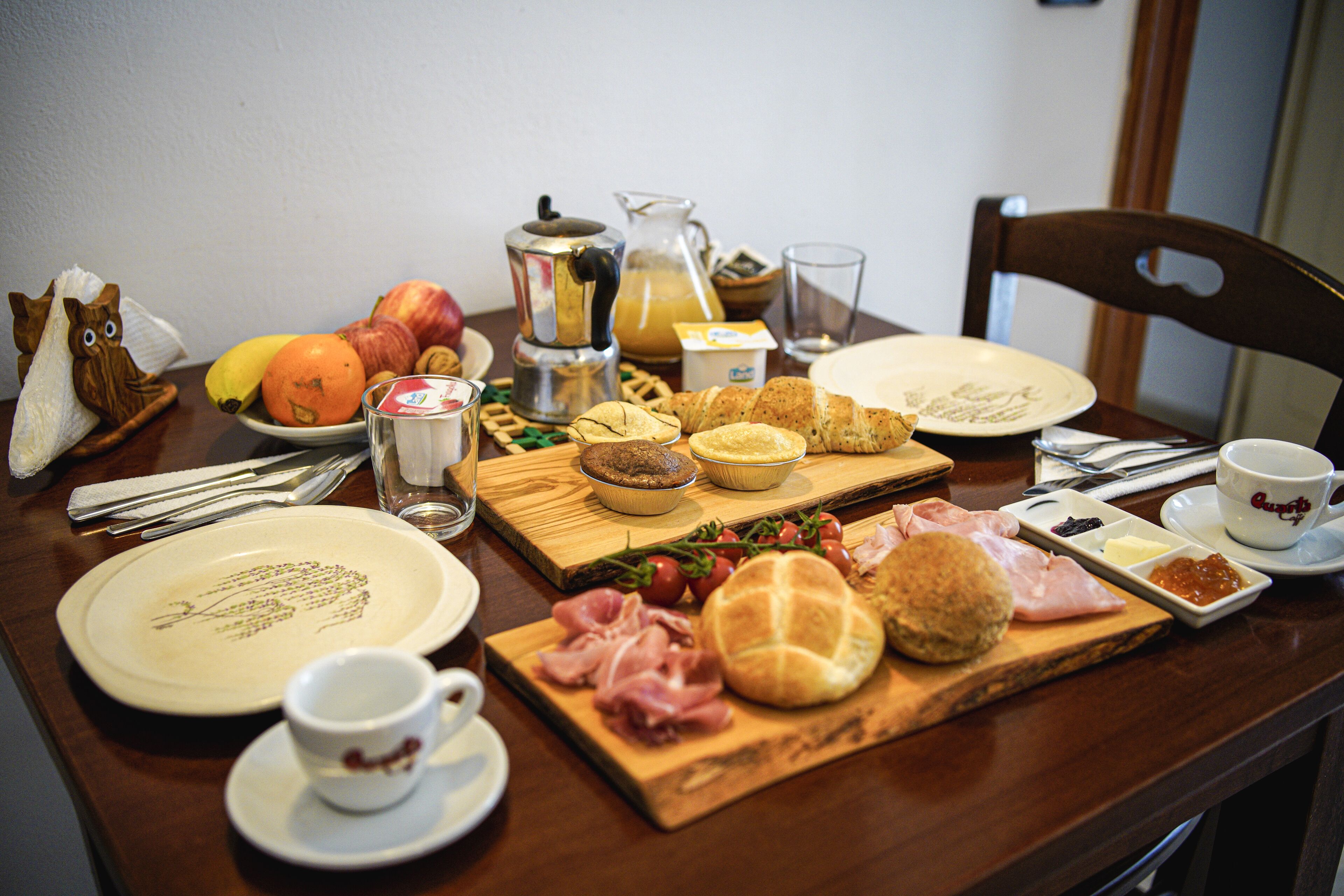 A breakfast table with various food items, plates, and cutlery.