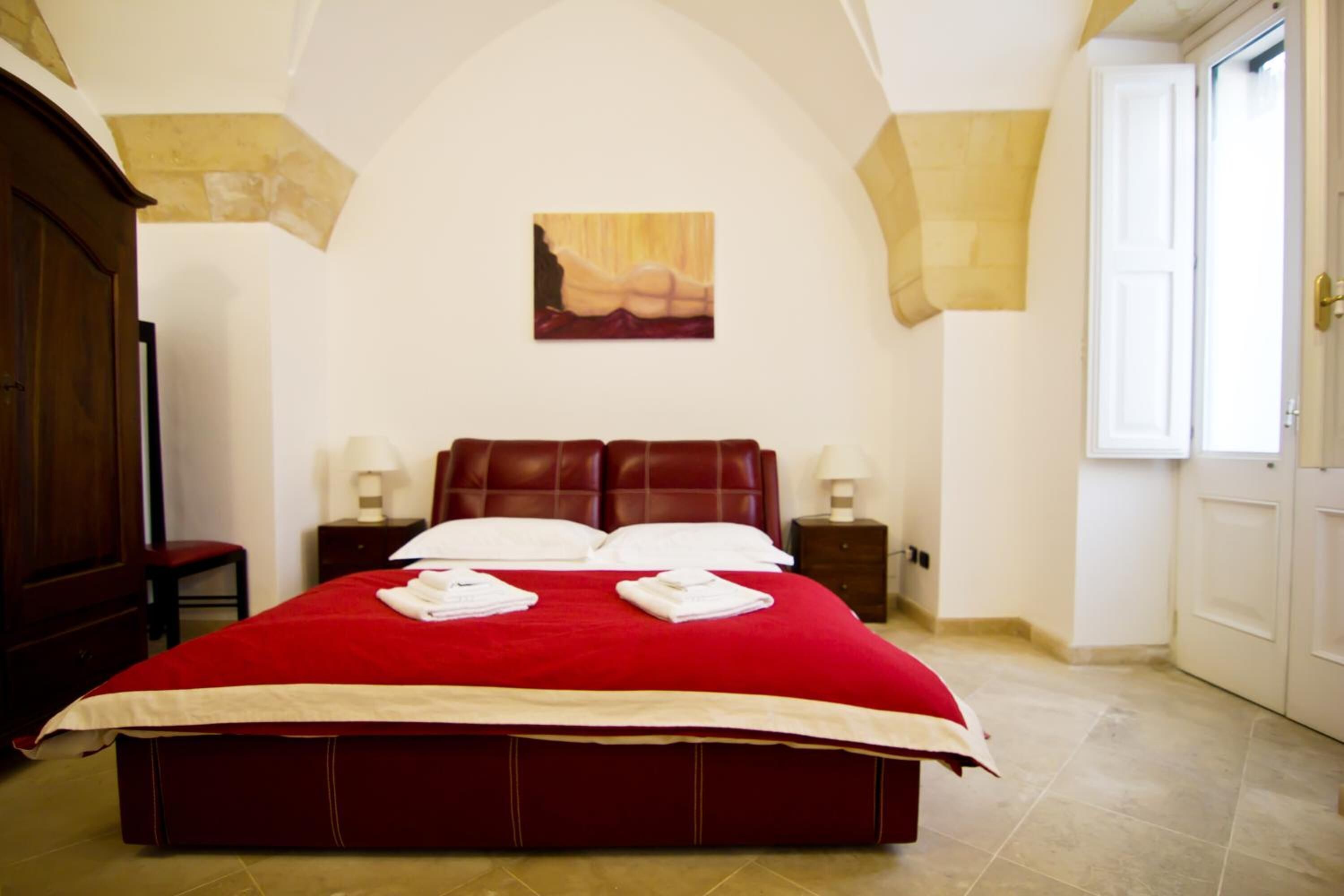 Une chambre d’hôtel avec un grand lit, un tableau au mur et une porte sur le côté droit.