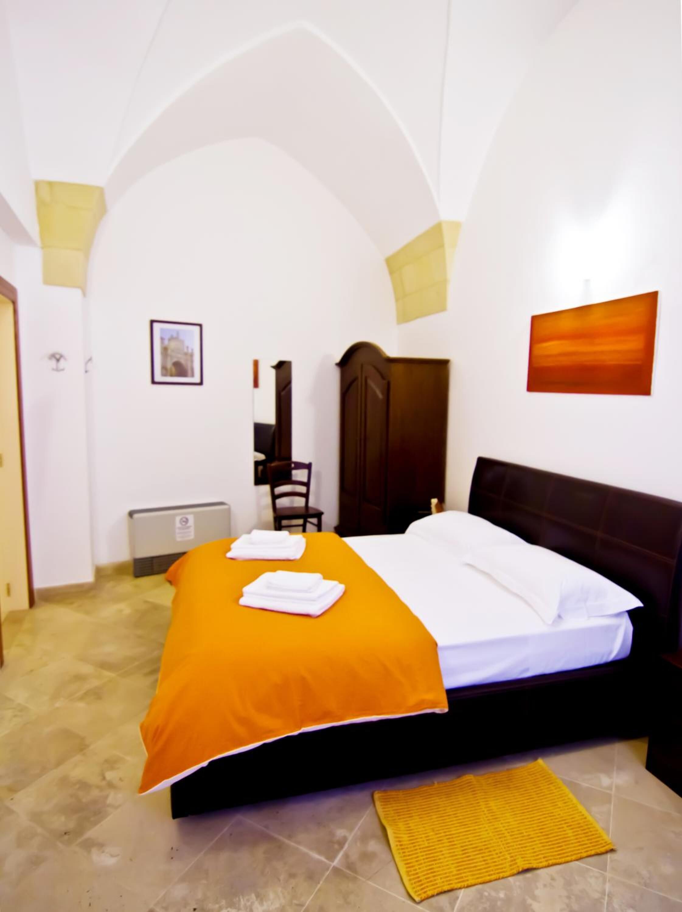 A hotel room with a bed, a chair, a wardrobe, a picture on the wall, and a radiator.