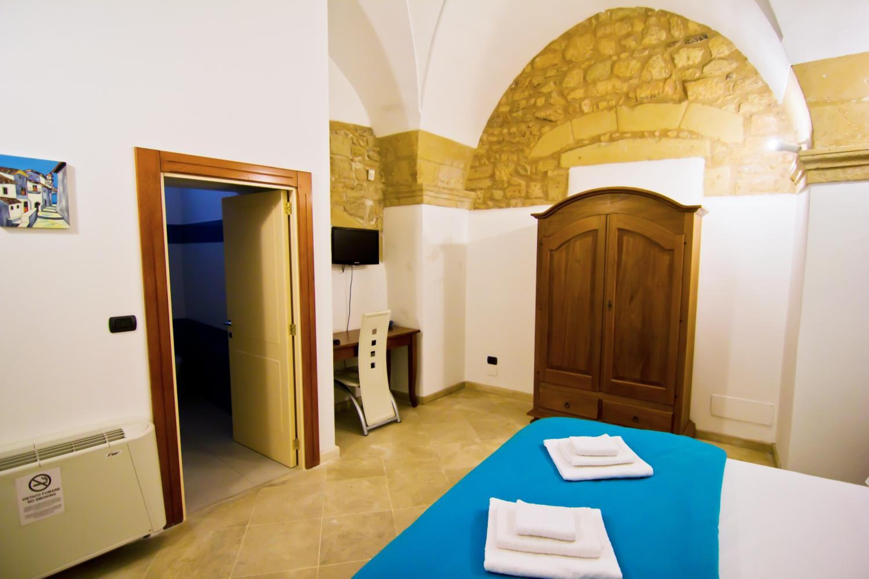Una habitación con una cama, un armario de madera, un escritorio y una pared de piedra.