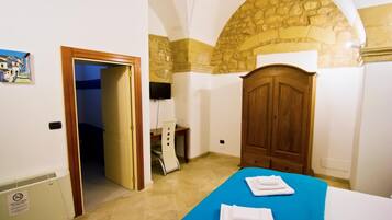 Una habitación con una cama, un armario de madera, un escritorio y una pared de piedra.
