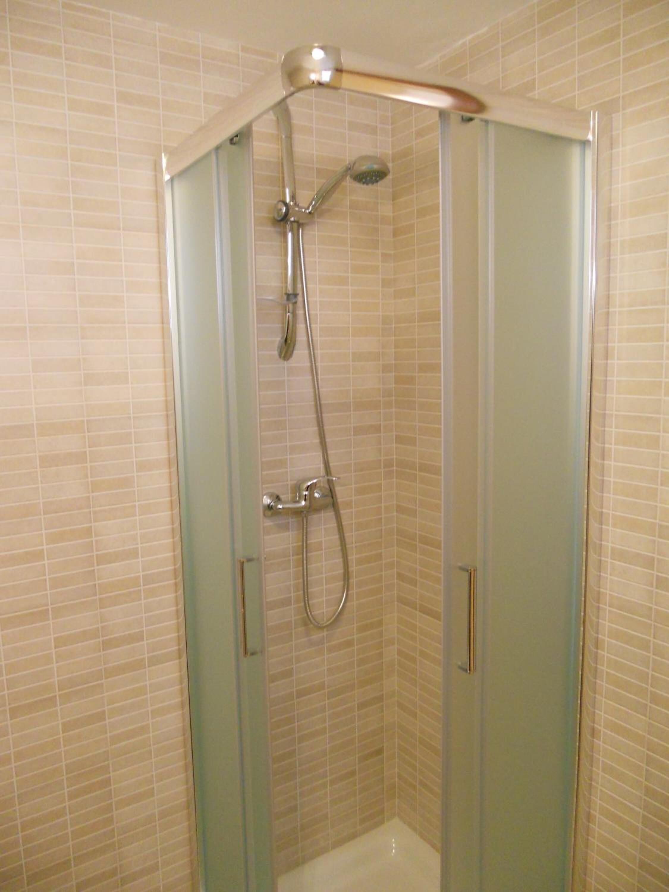 Ducha con cerramiento de vidrio, cabezal de ducha de mano y otro fijo en el techo.