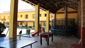 An outdoor covered patio with a foosball table, a swing set, and a trampoline. - Agriturismo La Mussia (Castelnuovo Calcea)