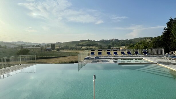 A swimming pool with clear water, surrounded by a stone deck and metal railings. There are several lounge chairs along the poolside. - Agriturismo La Mussia (Castelnuovo Calcea)