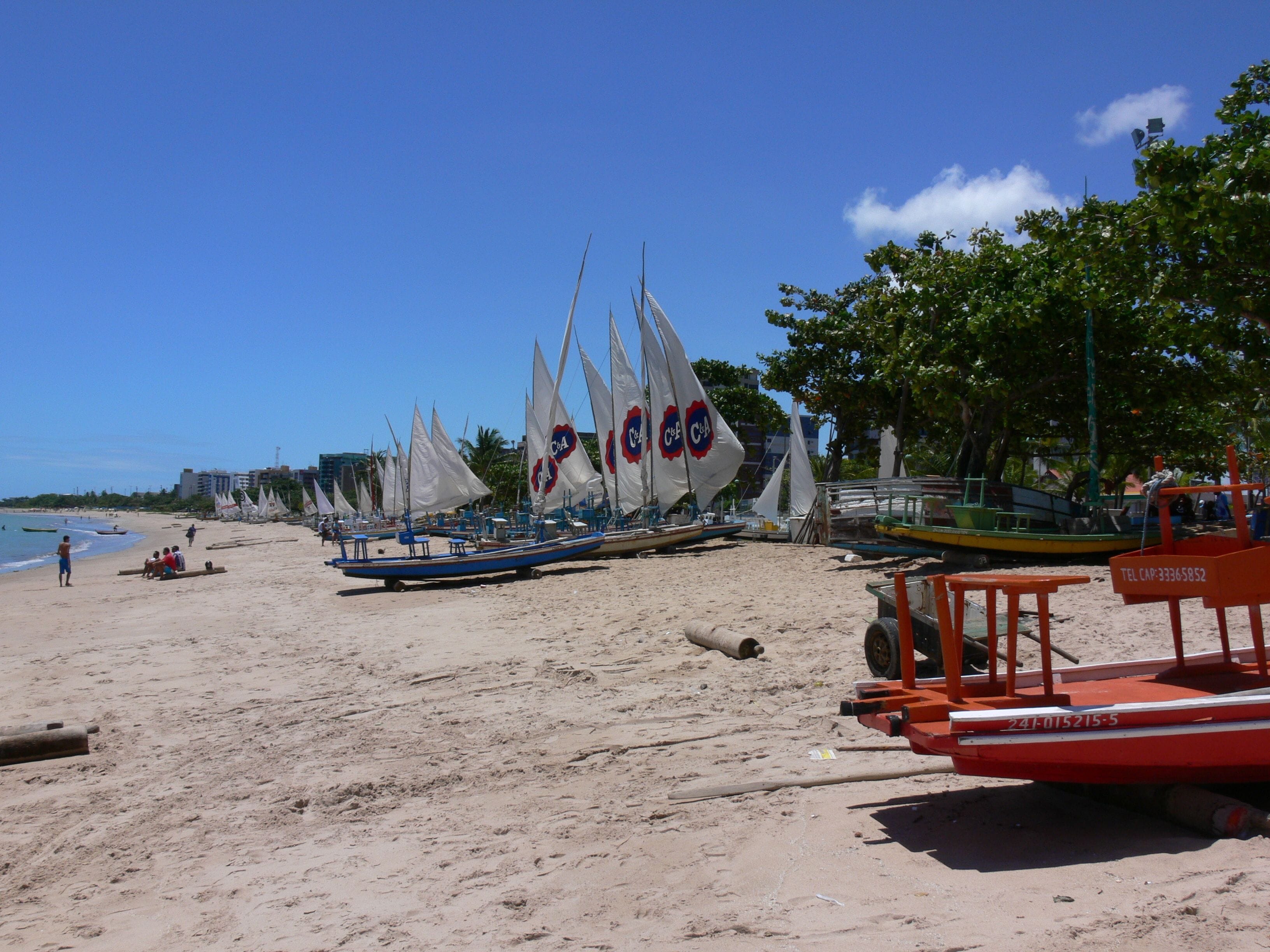 A beach with several sailboats docked, a lifeguard tower, and a clear blue sky.